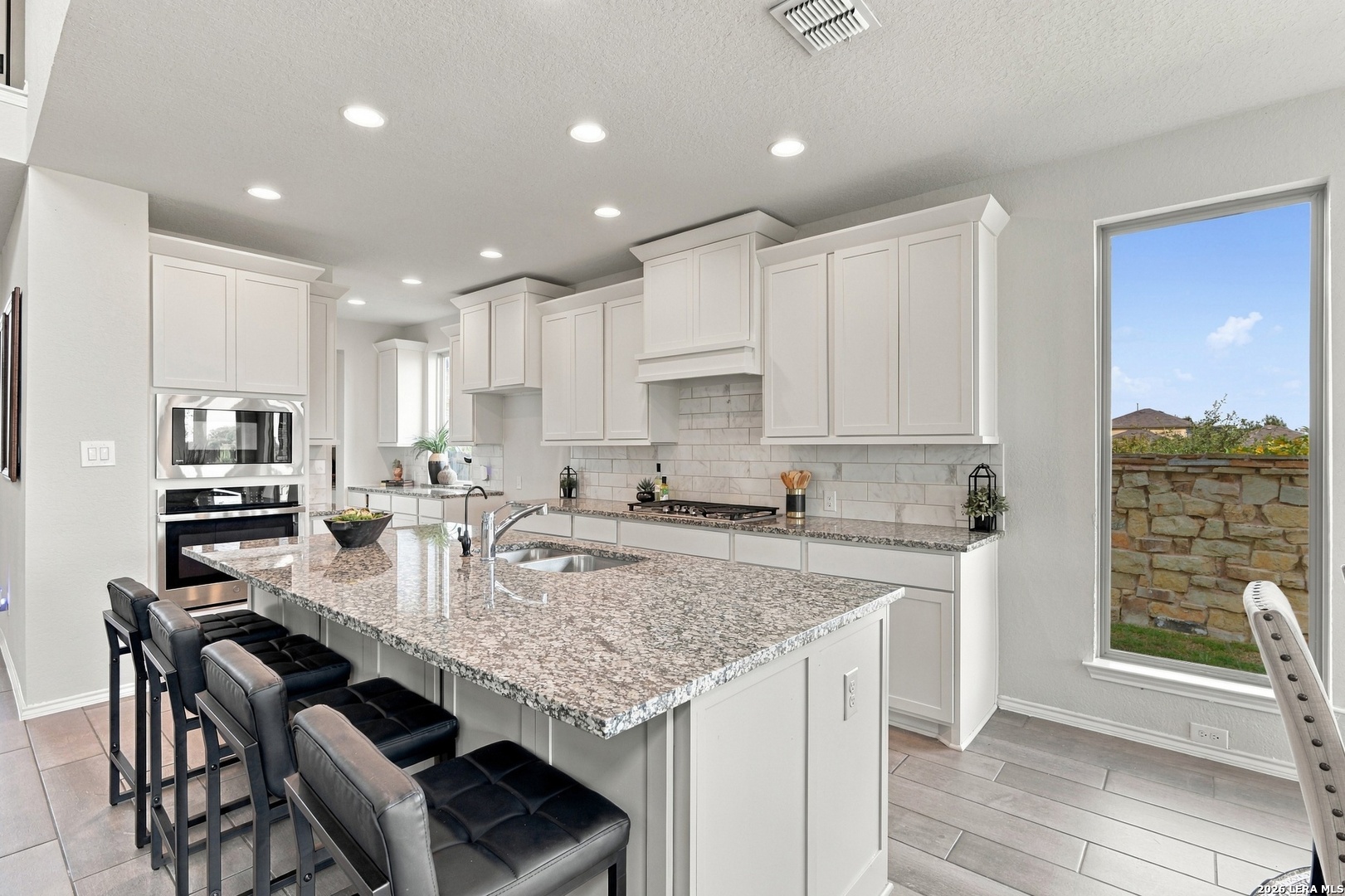 Kitchen with white cabinets, a large granite island, black bar stools, and stainless steel appliances.