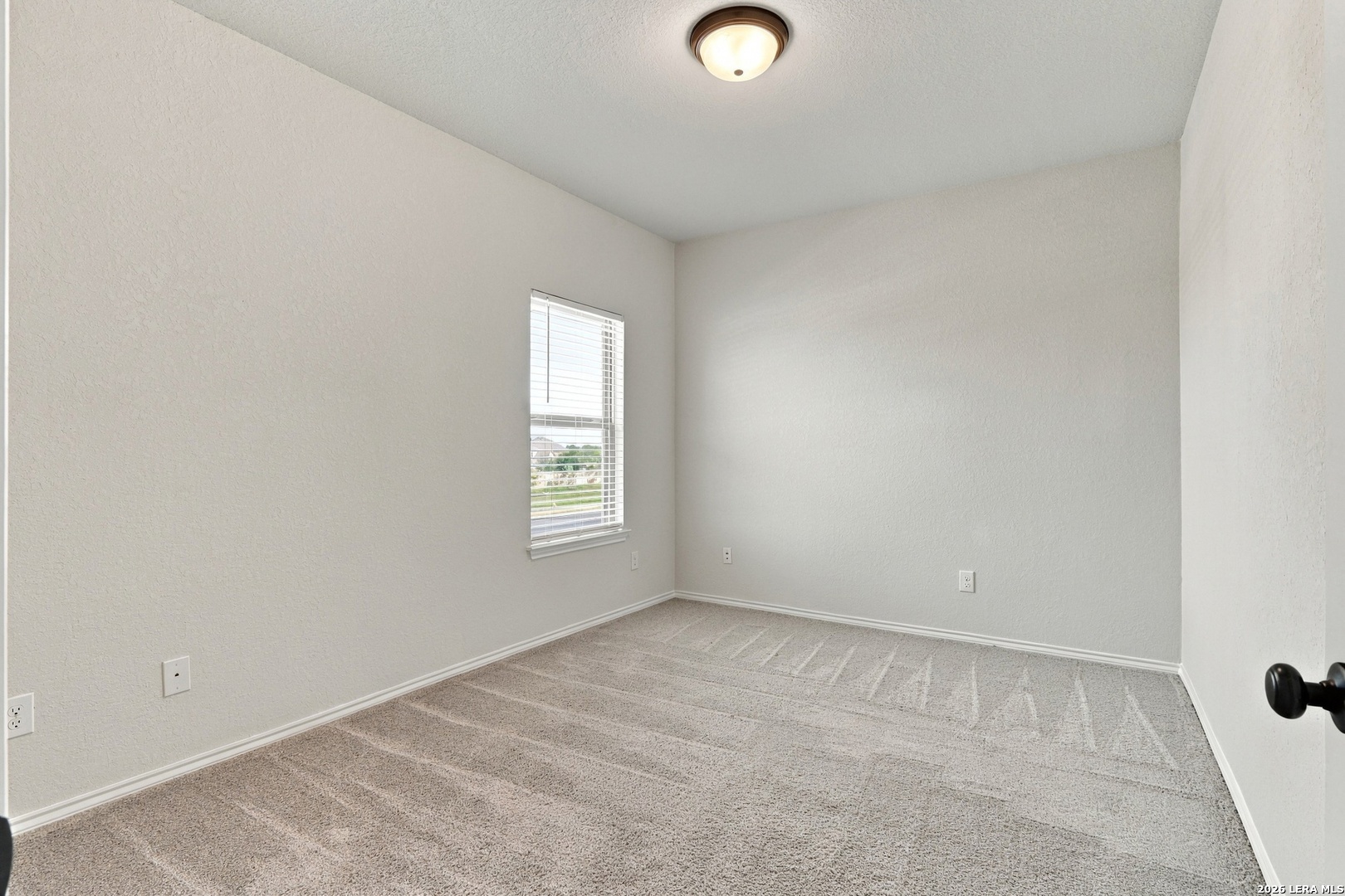 Empty bedroom with beige carpet, white walls, and a window with blinds.