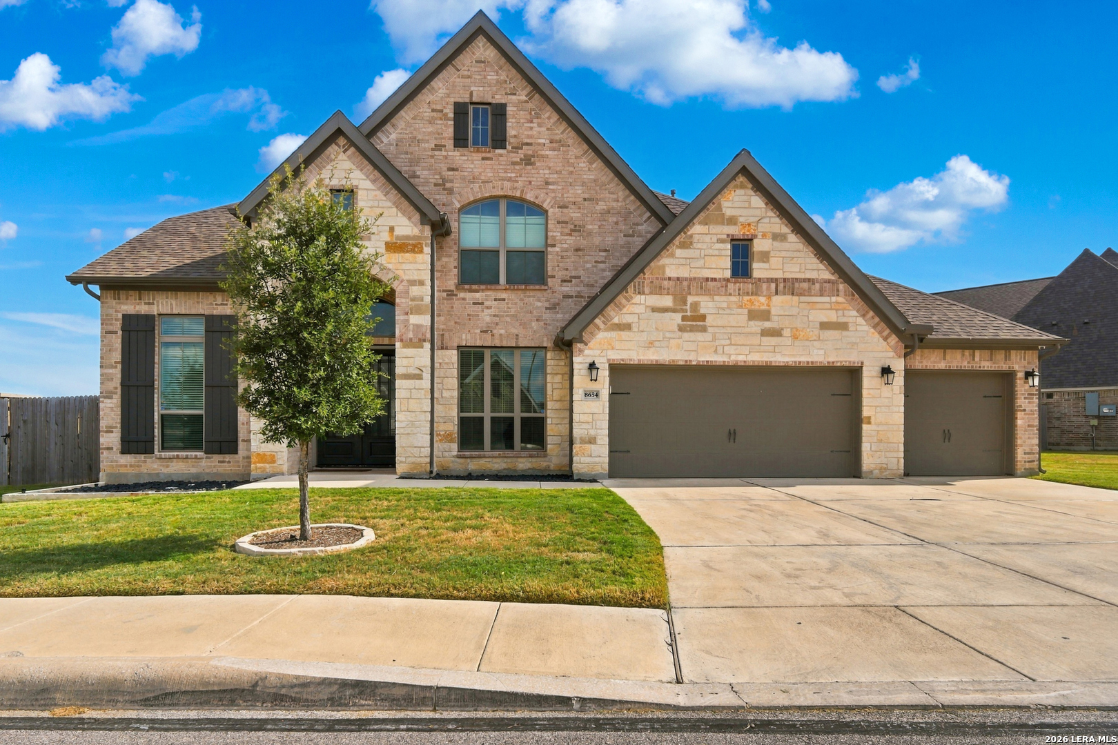 Two-story stone-and-brick house with multiple gables, dark shutters, and a two-car garage.