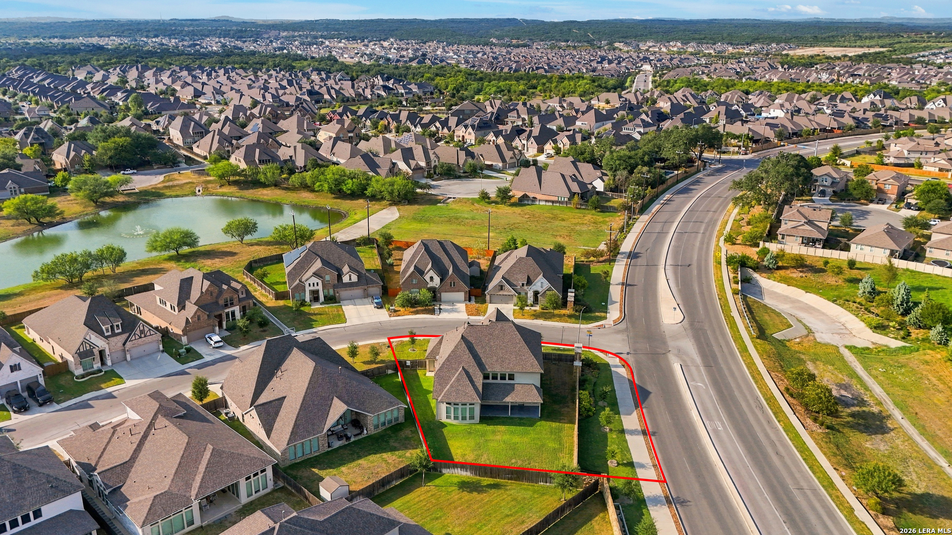 Aerial view of a two-story home and fenced lawn outlined in red beside a curving road.