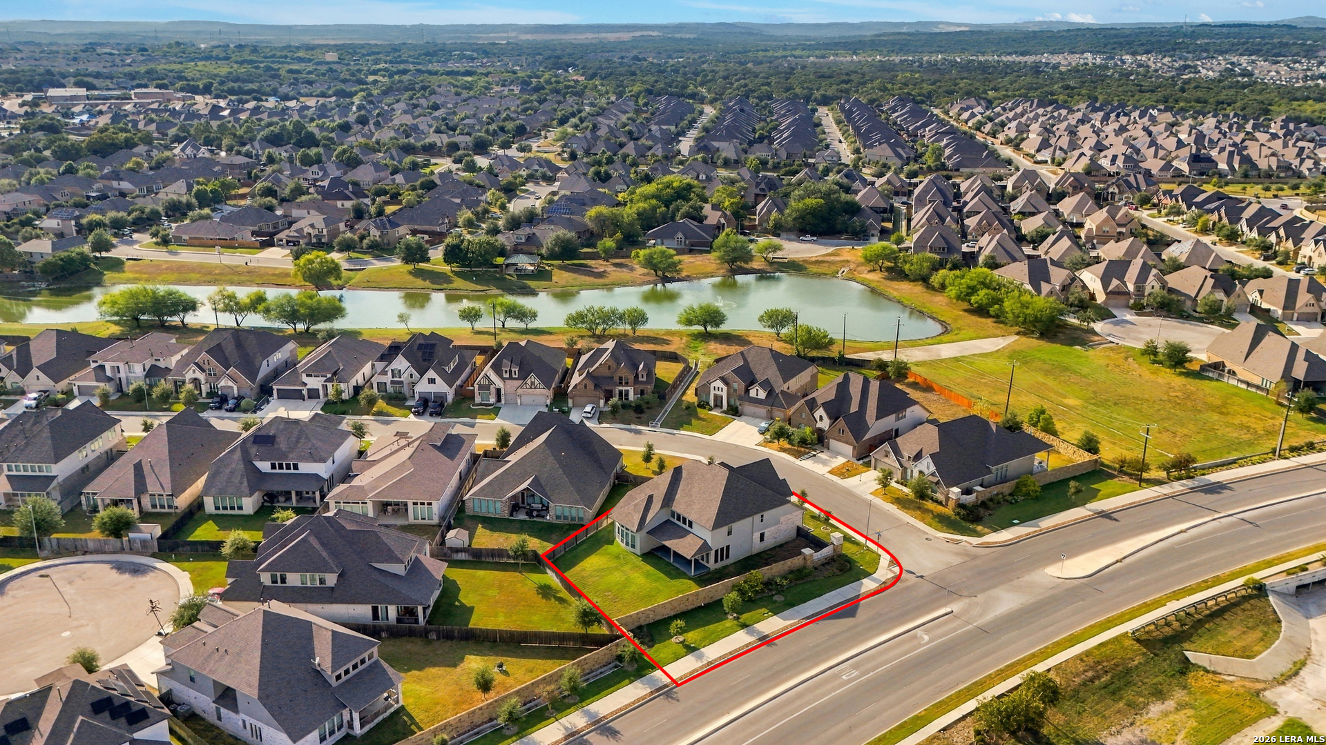 Aerial view of a corner-lot home outlined in red, with a neighborhood pond behind it.