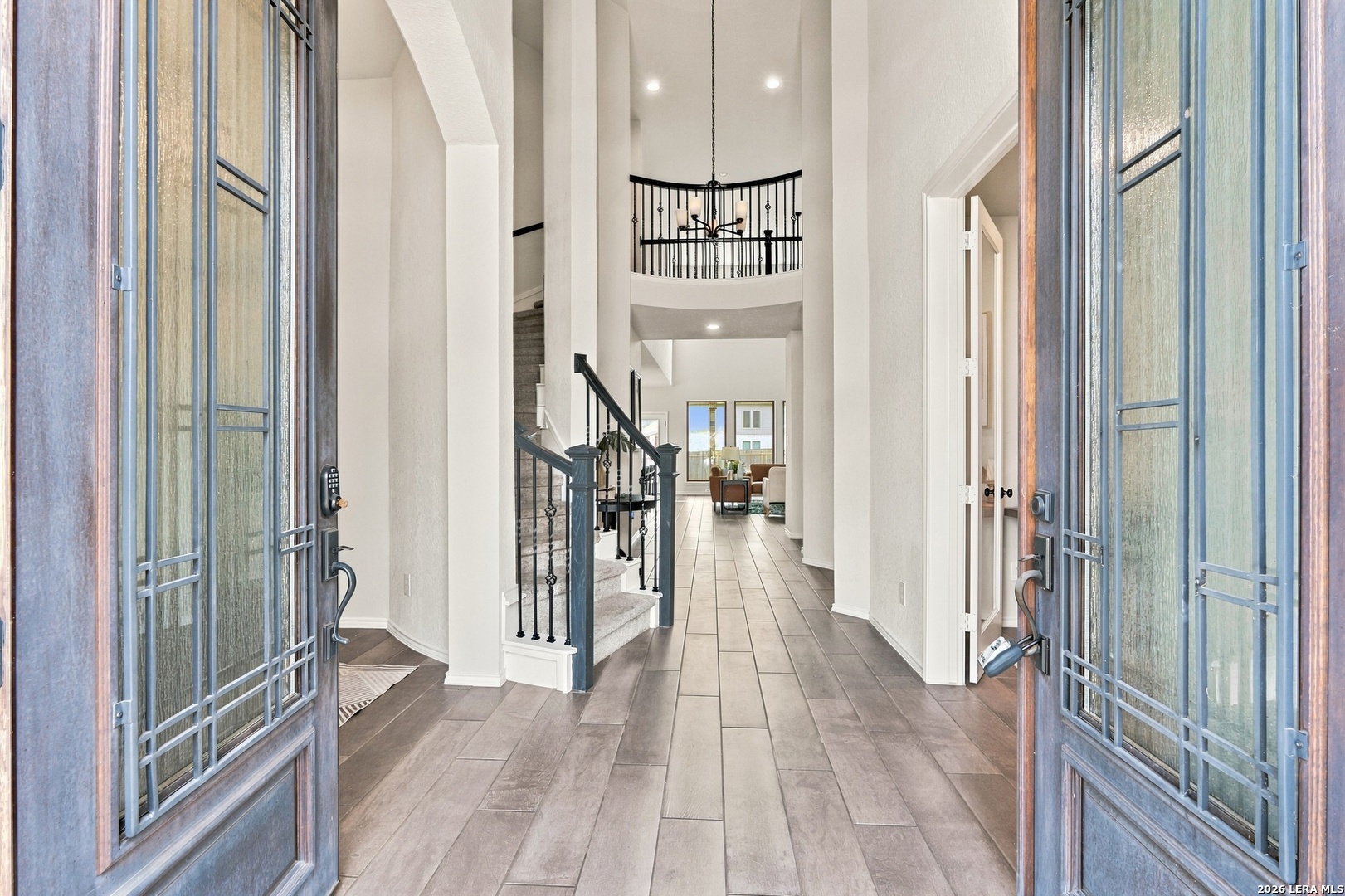 Two-story foyer with open front doors, tiled floors, iron stair railing, and a hanging chandelier.