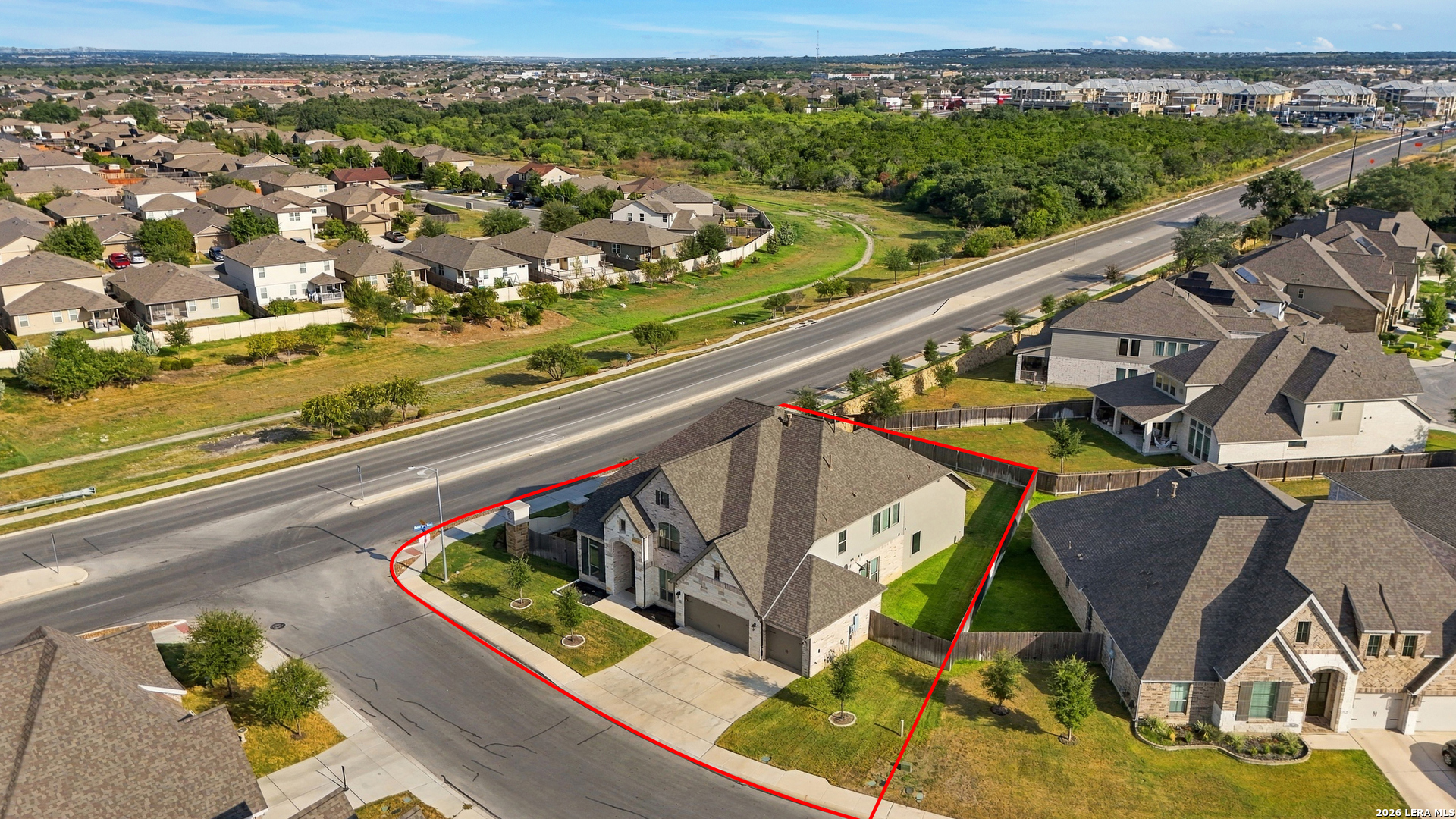 Aerial view of a corner-lot home outlined in red beside a broad road.