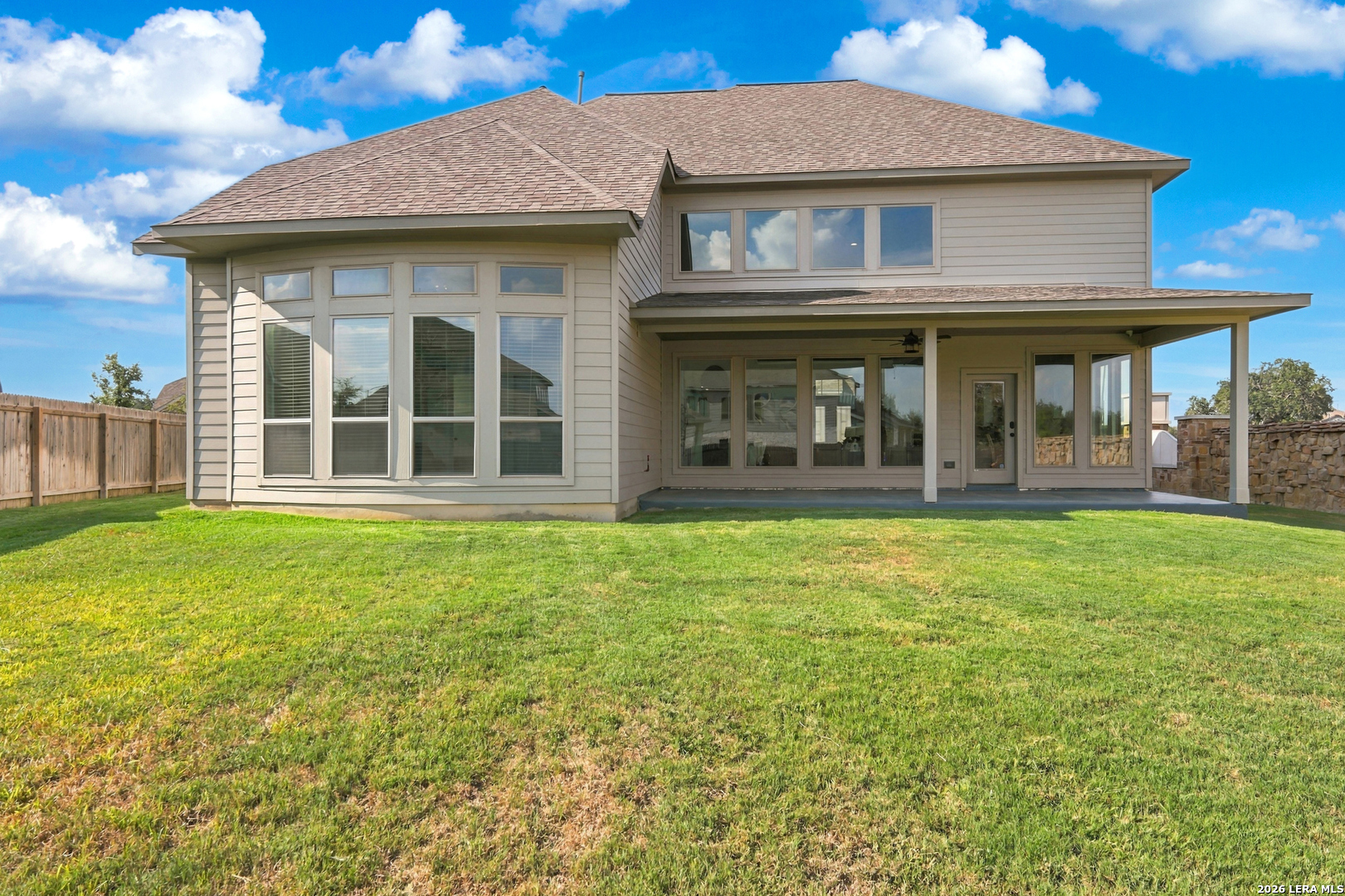 Rear of a two-story beige house with a covered patio and broad grassy backyard.