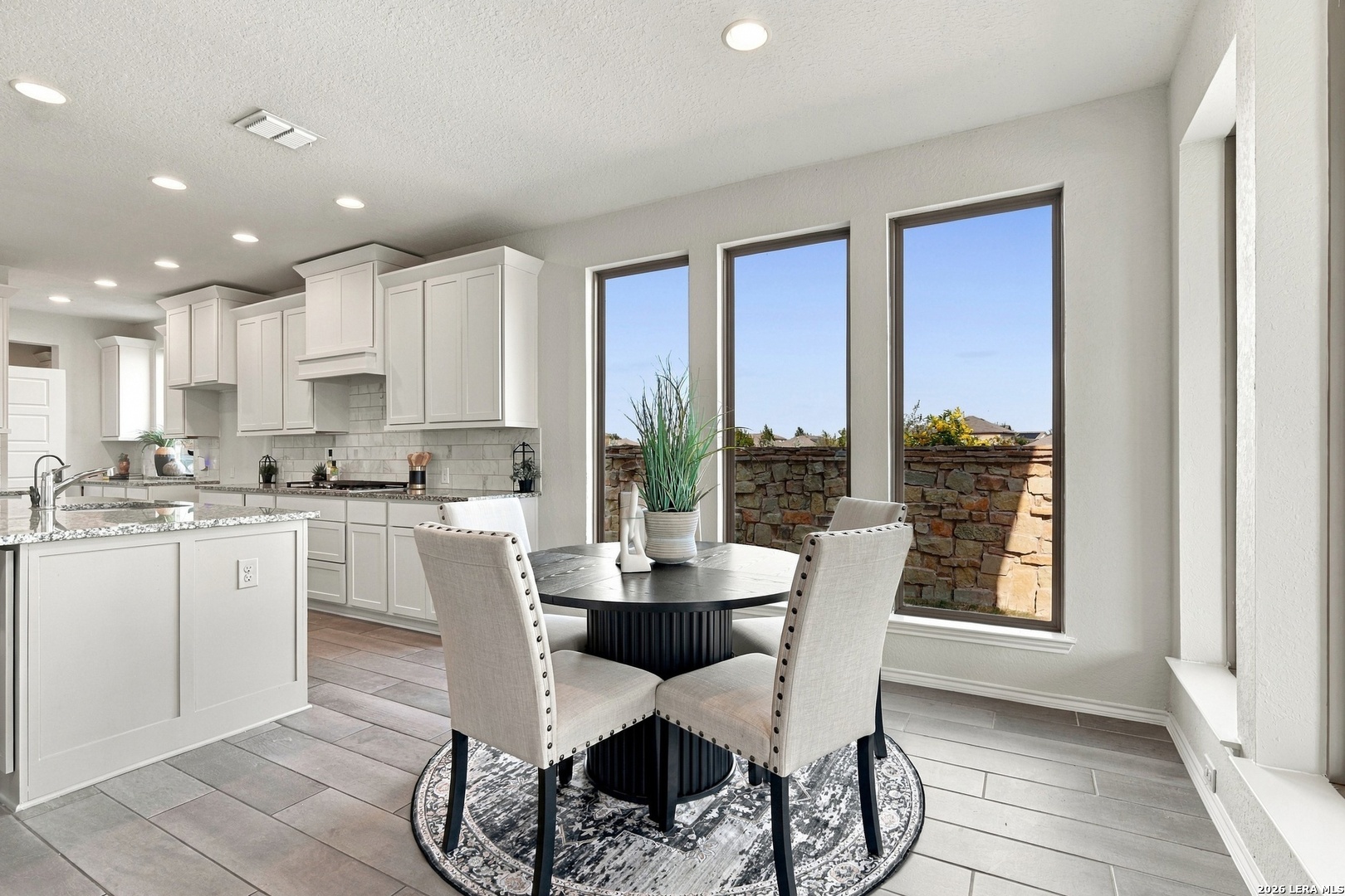 Kitchen and dining area with white cabinets, a granite island, and a round table by tall windows.