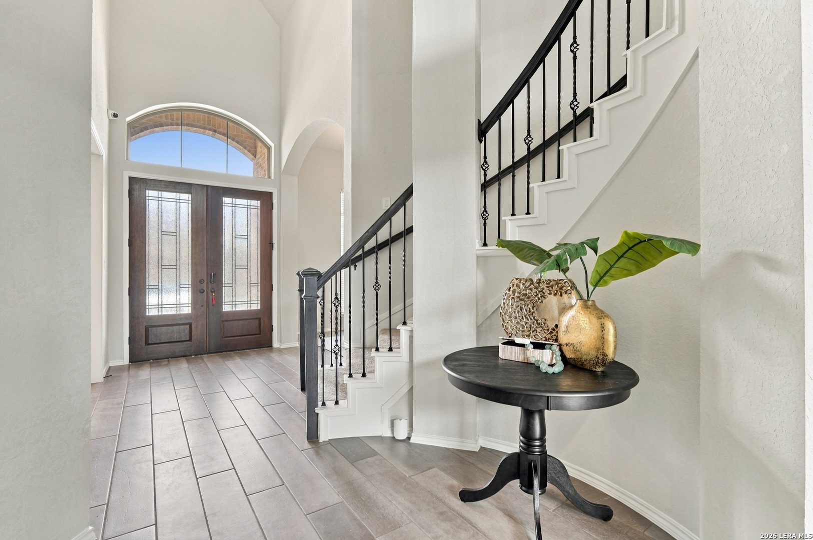 Entryway with arched double doors, tiled floor, and staircase with black metal railings.