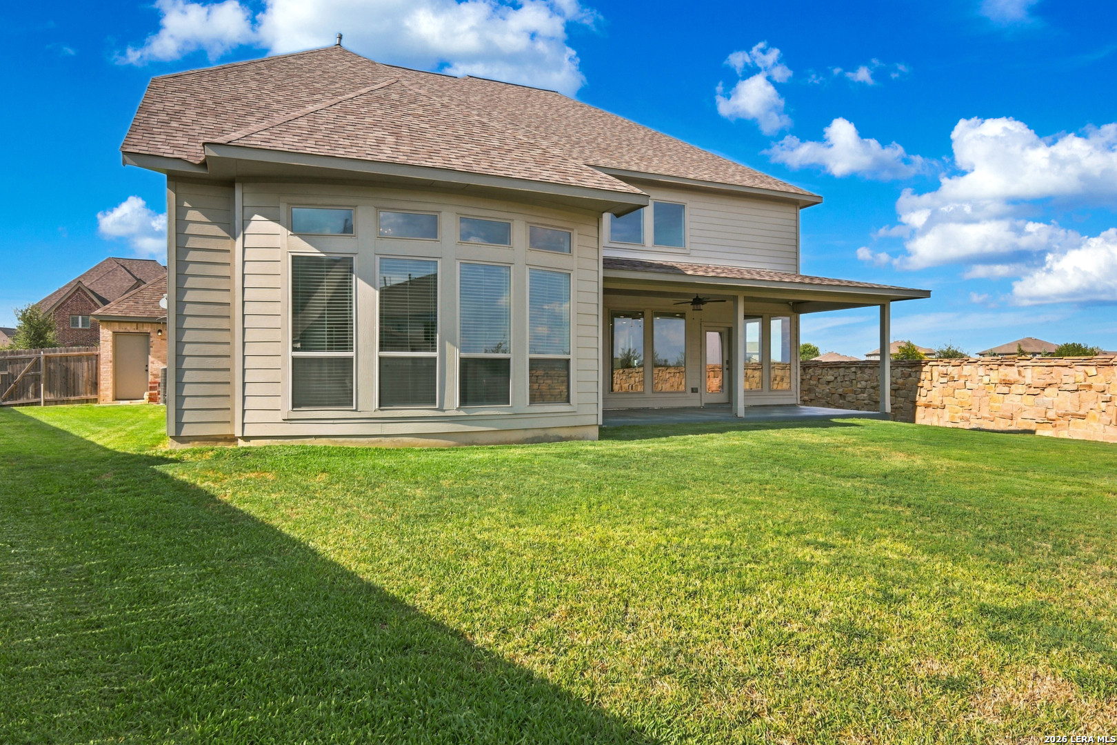 Rear of a two-story house with tall windows, a covered patio, and a broad lawn.