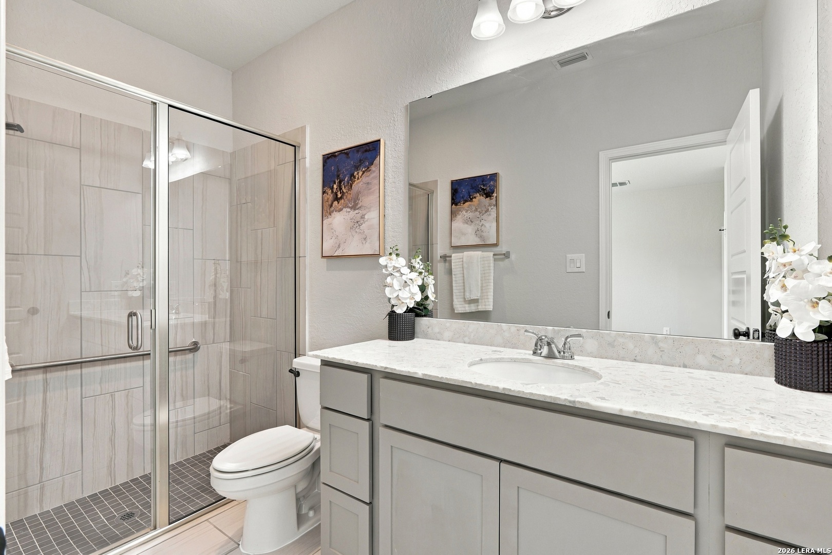 Bathroom with a glass-enclosed tiled shower and gray vanity with a white countertop.