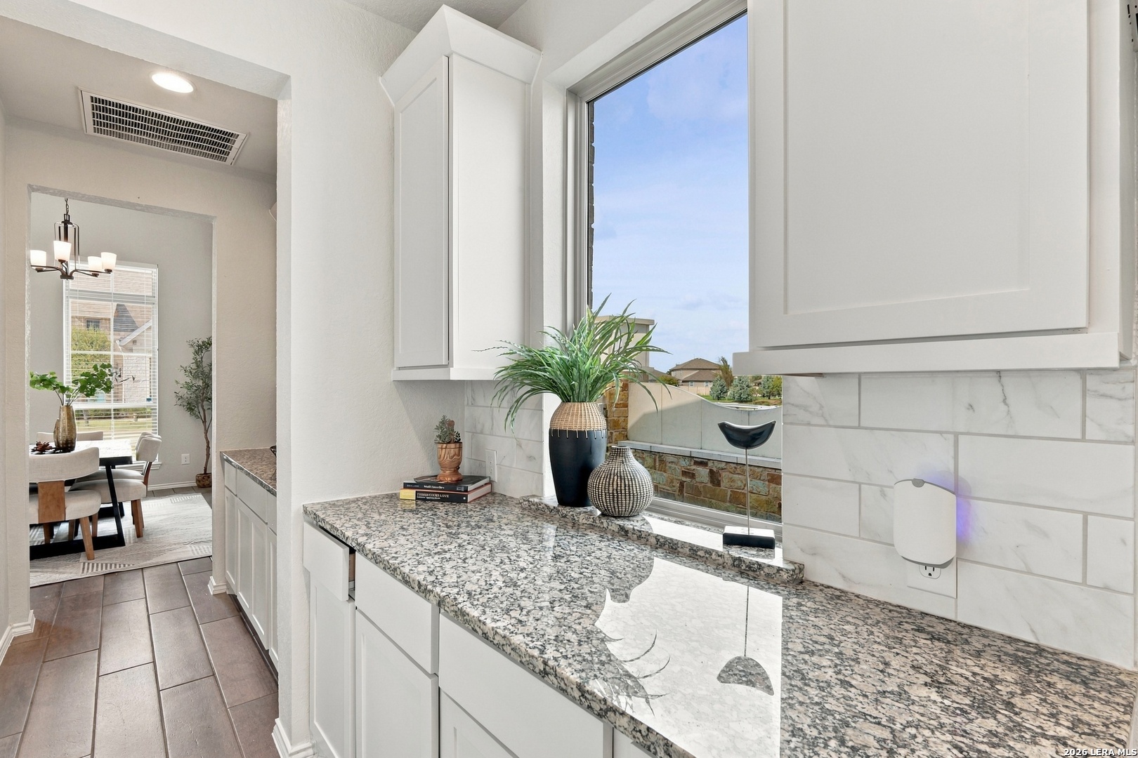 Kitchen with white cabinets, speckled granite counters, and a wide window overlooking neighboring homes.