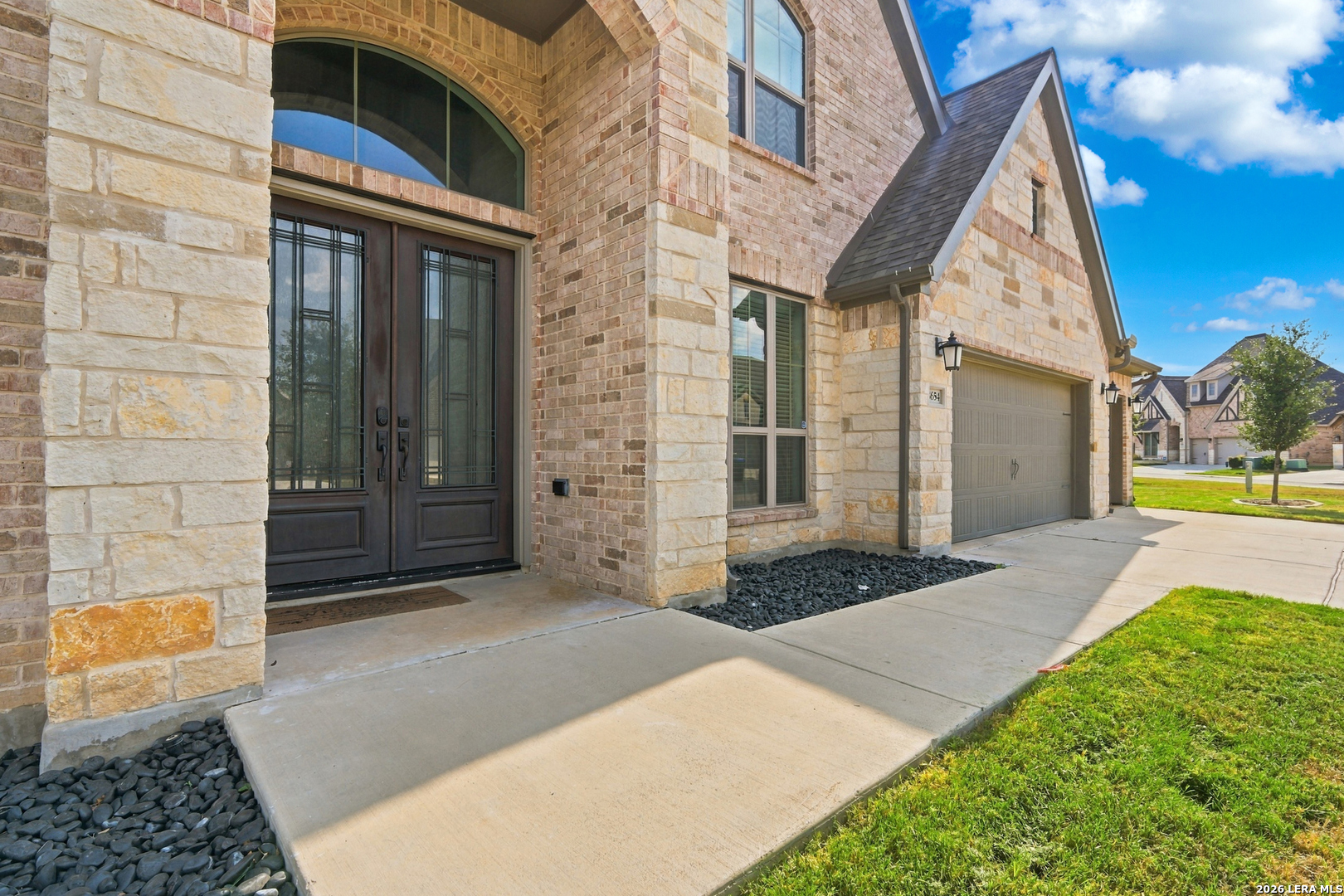Stone-and-brick home with an arched double-door entry, attached garage, and landscaped rock beds.