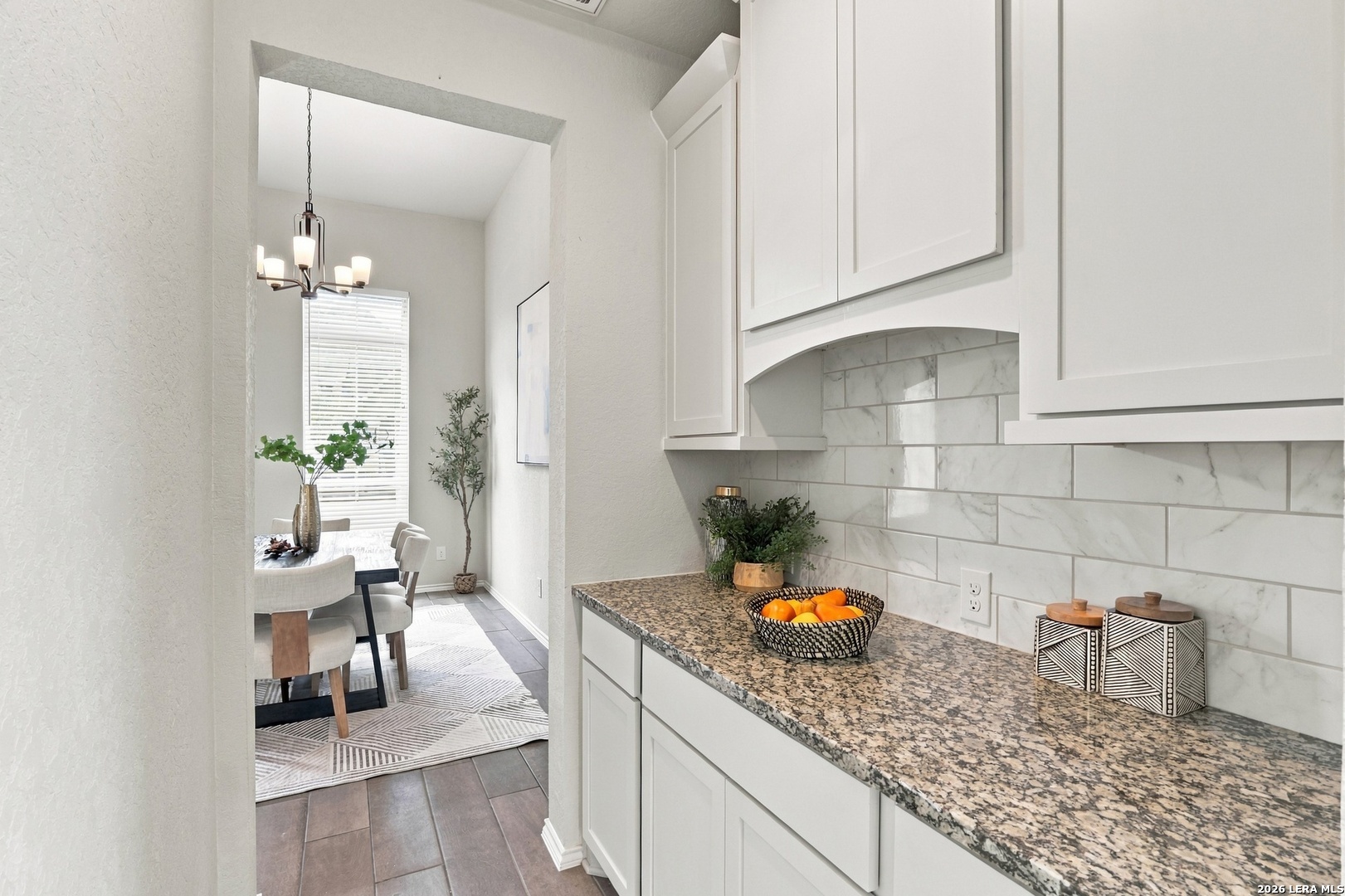 Staged kitchen with white cabinets, granite counters, and a view into the dining area.