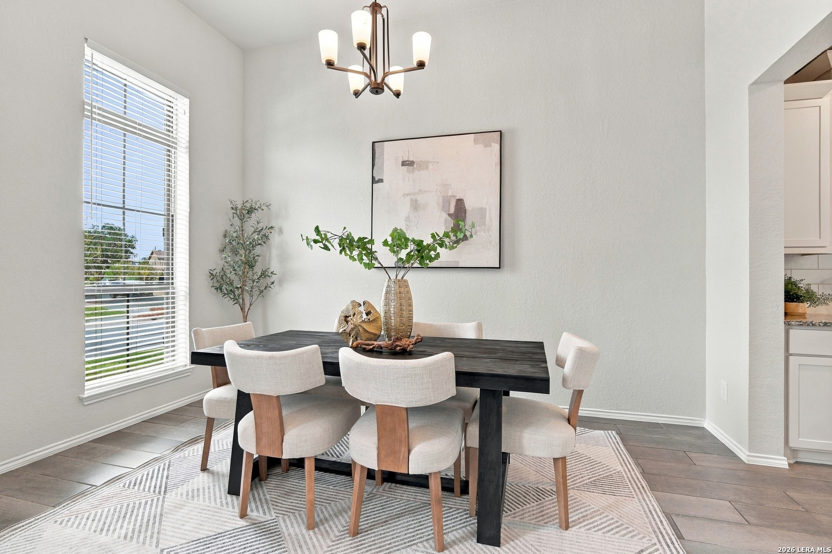 Staged dining room with a dark table, upholstered chairs, geometric rug, and large window.