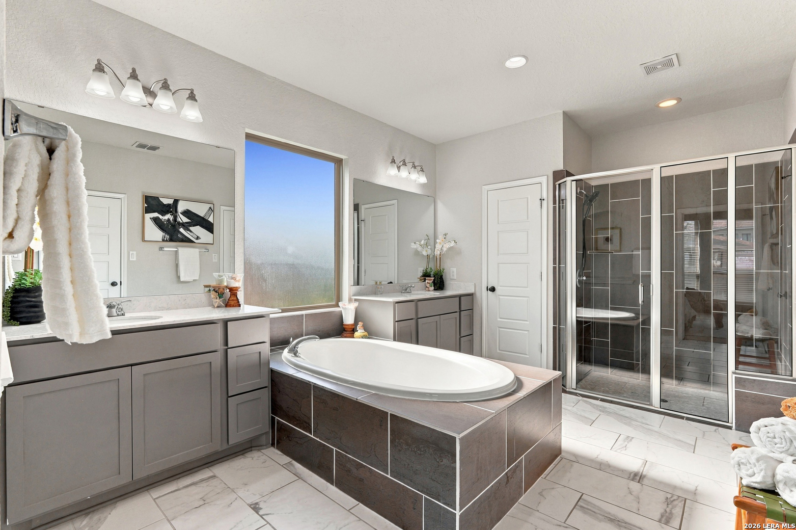 Primary bathroom with a tiled soaking tub, gray double vanities, and a glass-enclosed shower.