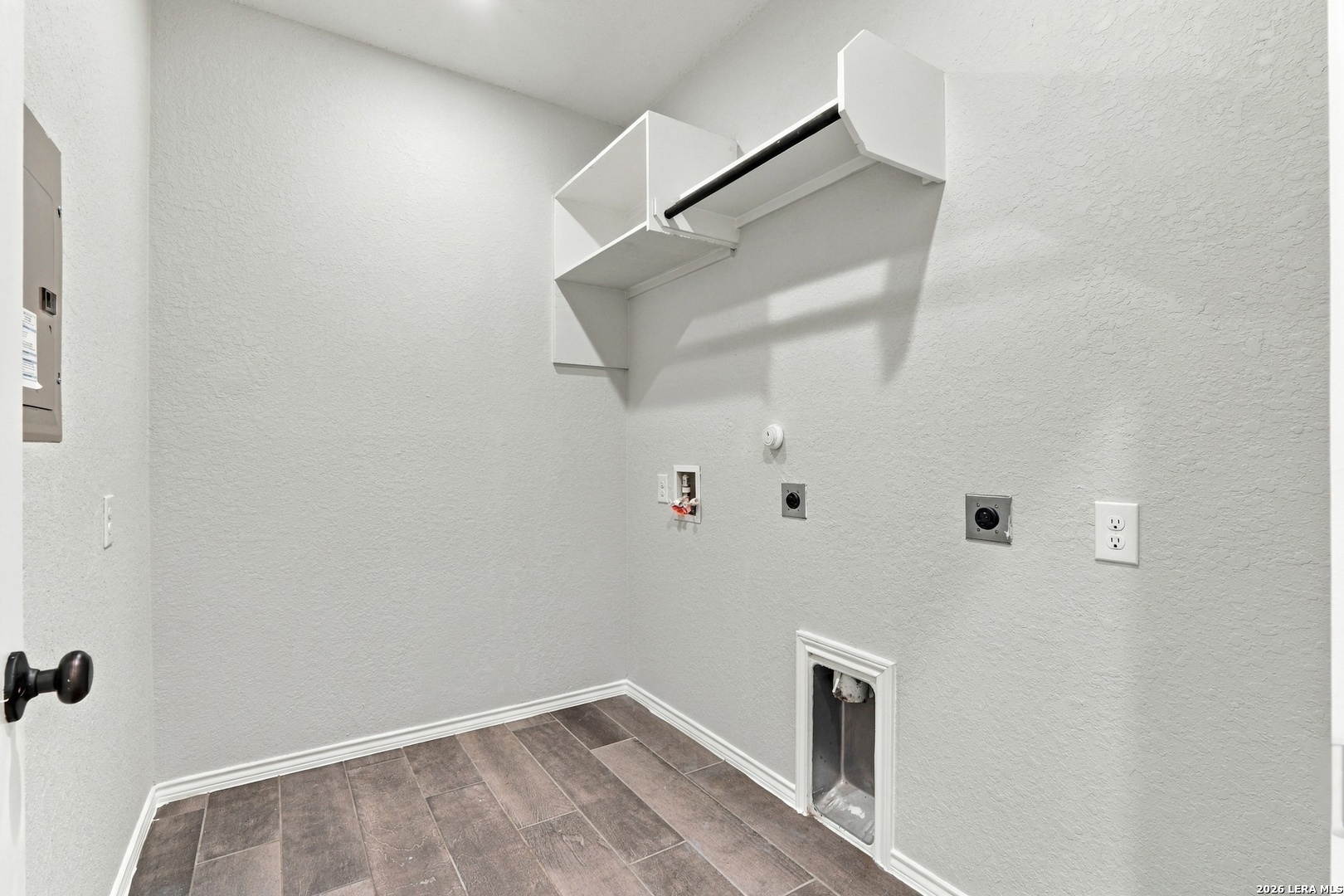Empty laundry room with washer and dryer hookups, a high shelf, and brown tile flooring.