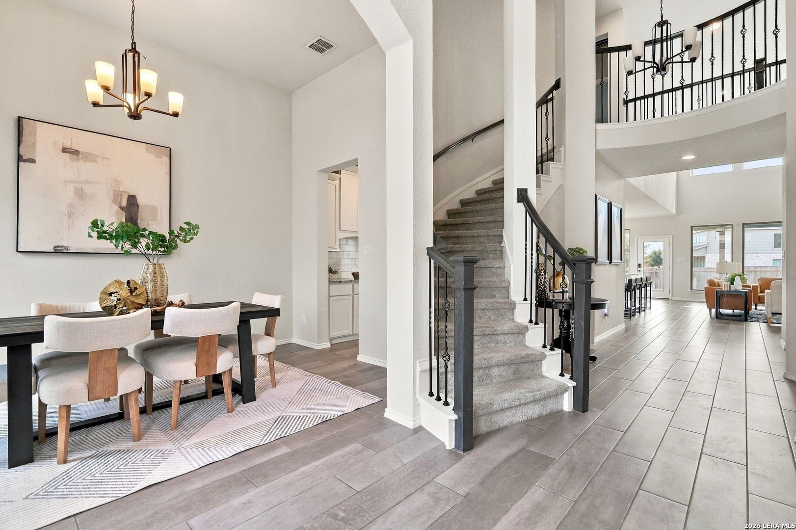 Furnished dining area beside a carpeted staircase with black iron railing.