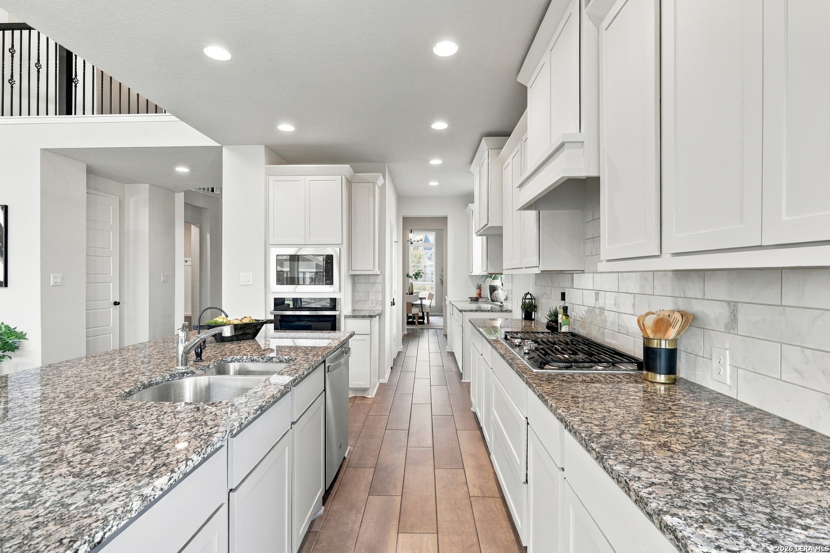 Bright kitchen with white cabinets, granite counters, a large sink island, and a gas cooktop.