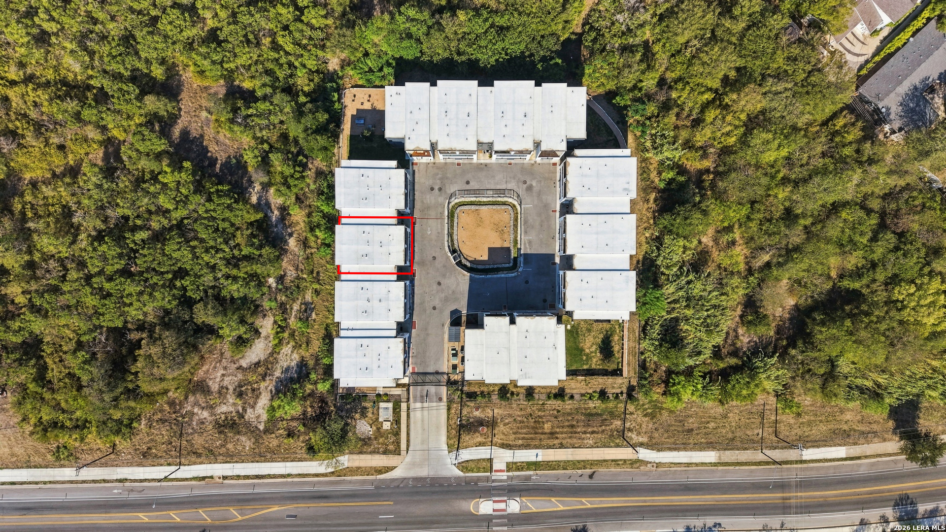 Aerial view of a residential complex with one unit outlined in red, surrounded by trees.