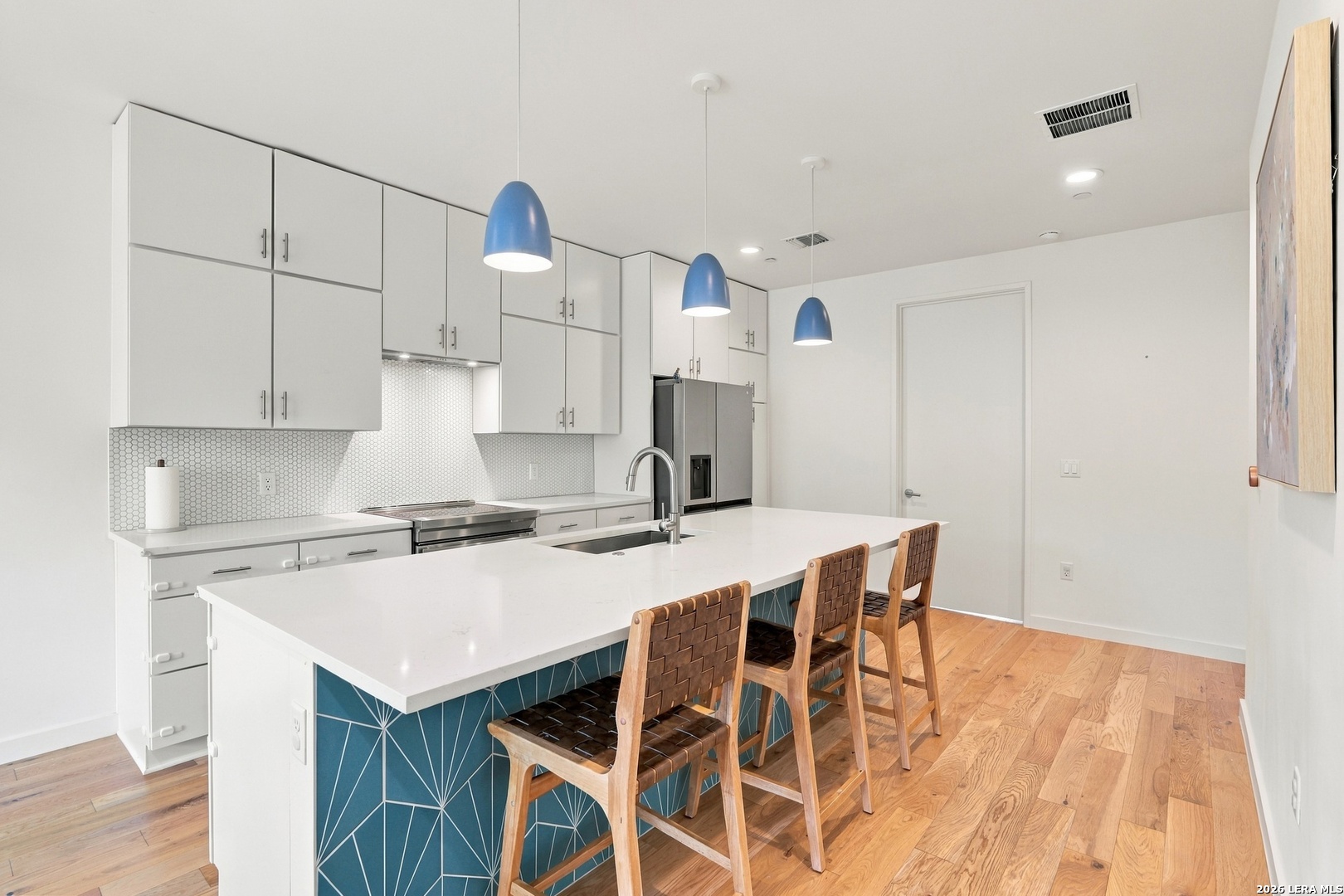 Modern kitchen with a blue geometric-tile island, wooden bar stools, white cabinetry, and hardwood floors.