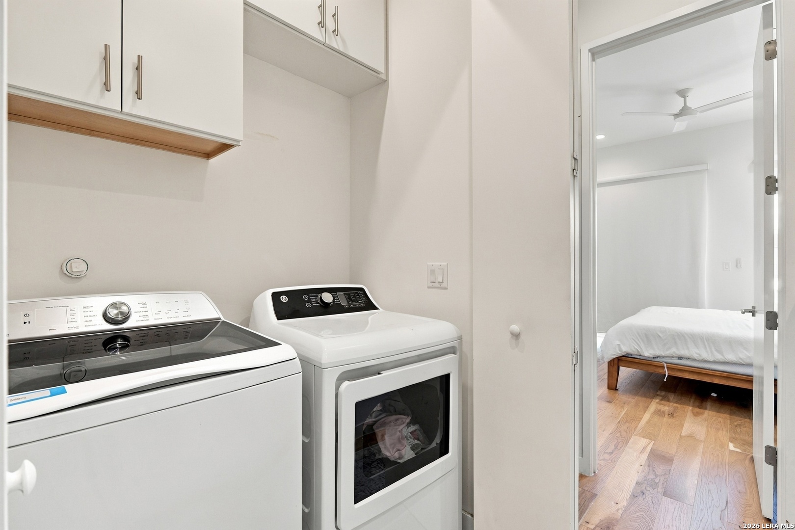 Laundry room with washer and dryer, opening onto a bedroom with hardwood floors.