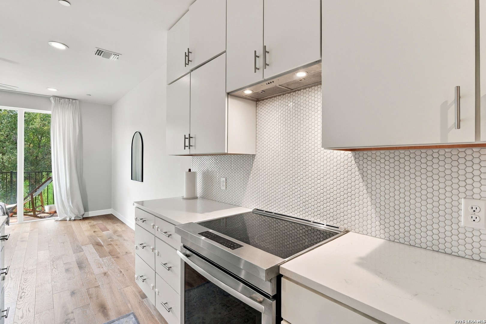 Modern kitchen with white cabinets, hexagonal tile backsplash, stainless steel range, and a balcony door.