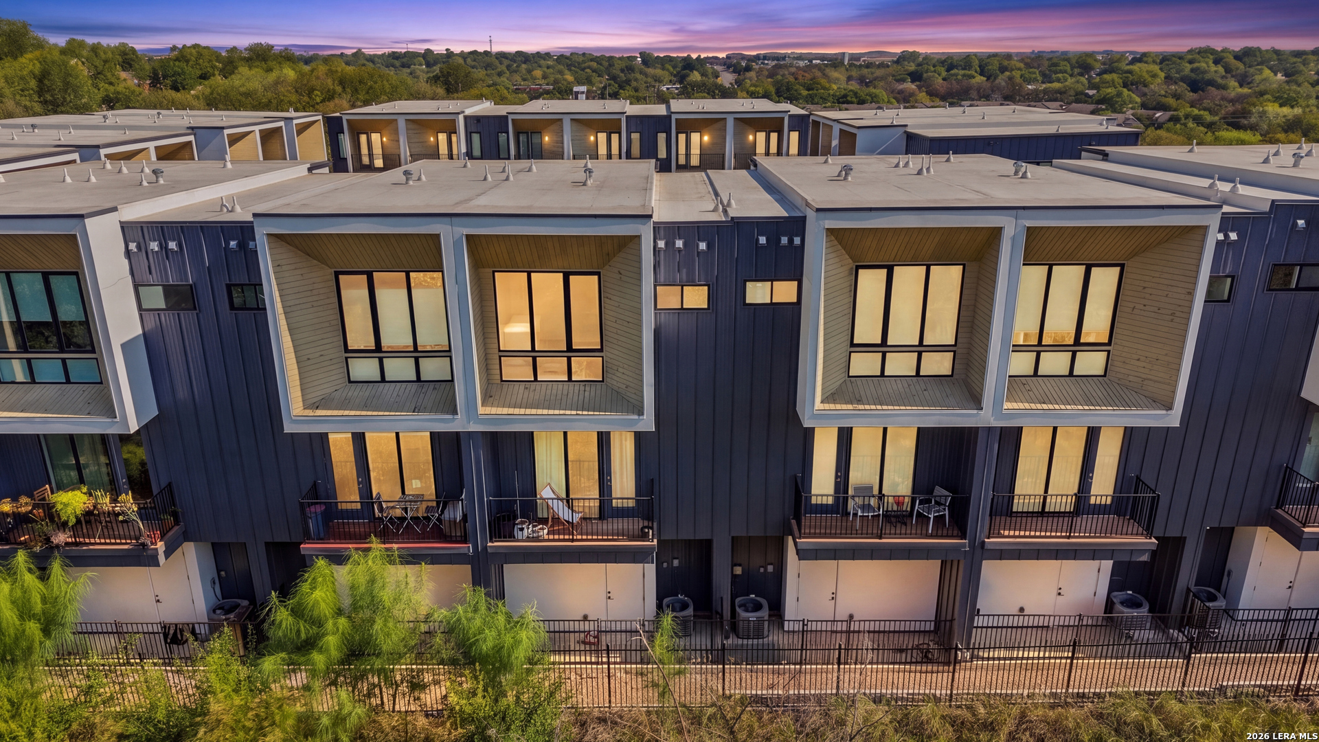 Modern multi-unit building with projecting window bays and balconies, viewed aerially at dusk.