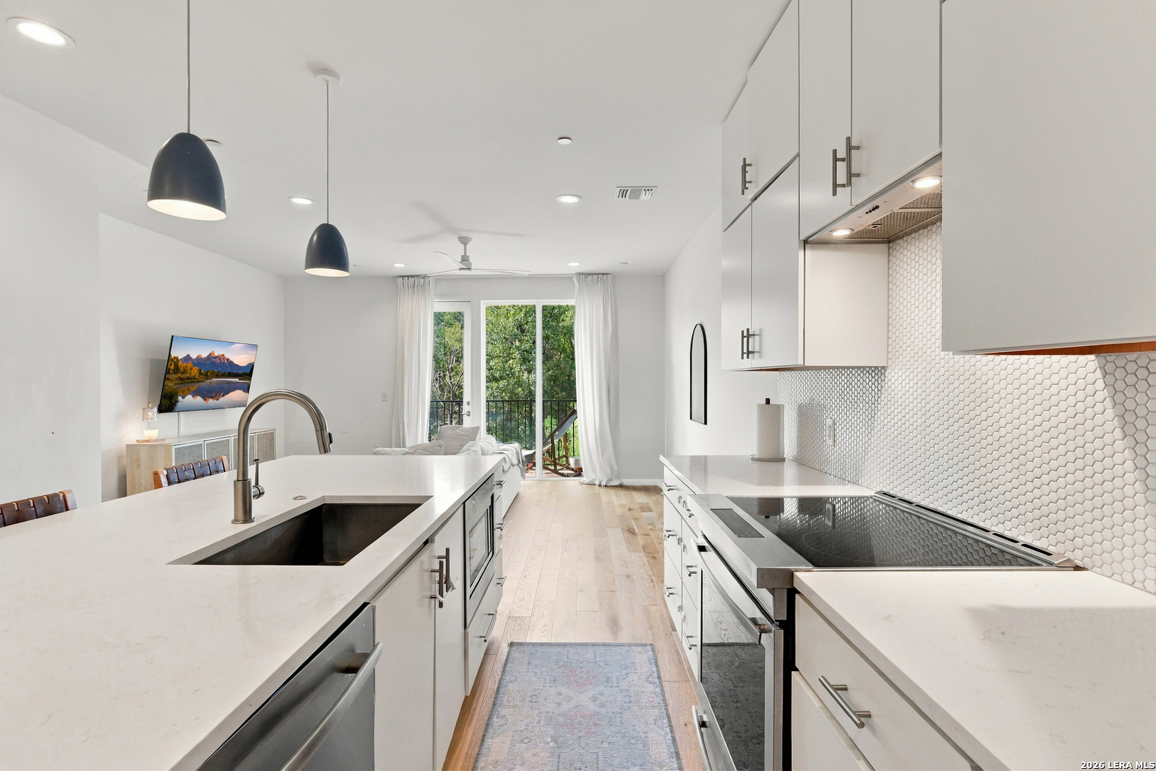 Modern white kitchen with a large island, geometric tile backsplash, and balcony doors overlooking trees.