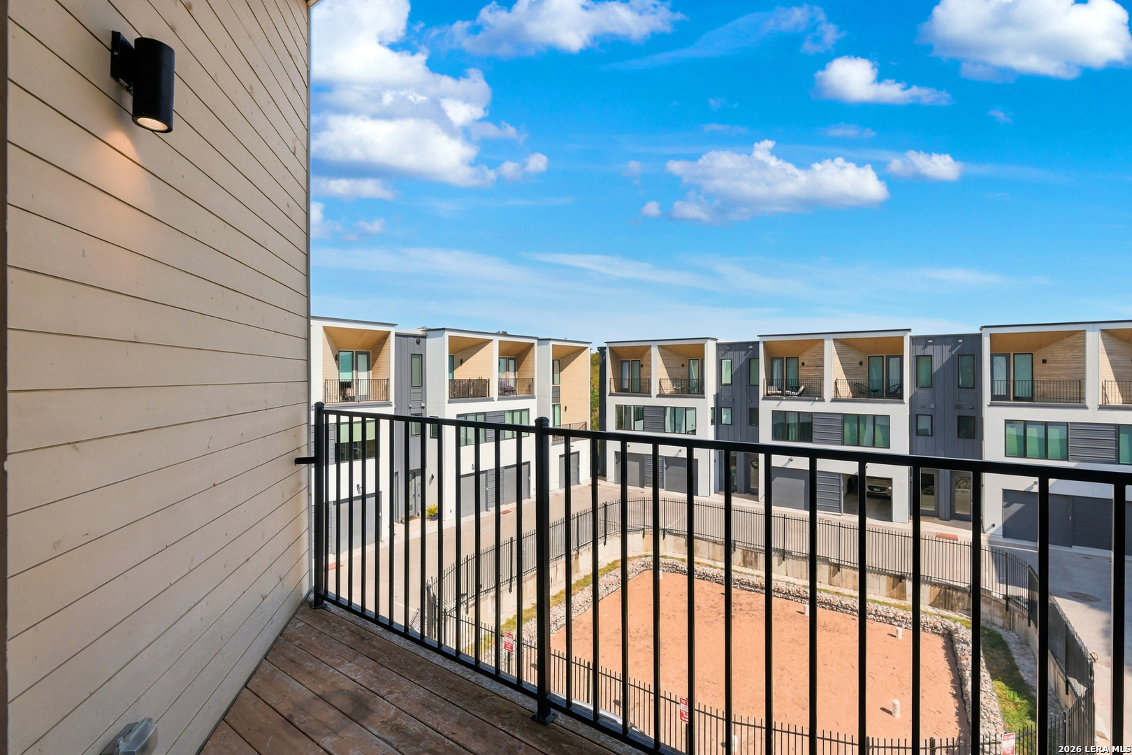 Balcony with black railing overlooking modern townhomes and a fenced courtyard.