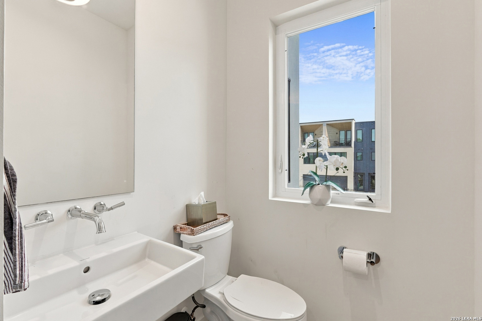 Modern bathroom with a large white sink, chrome fixtures, and an orchid on the window ledge.