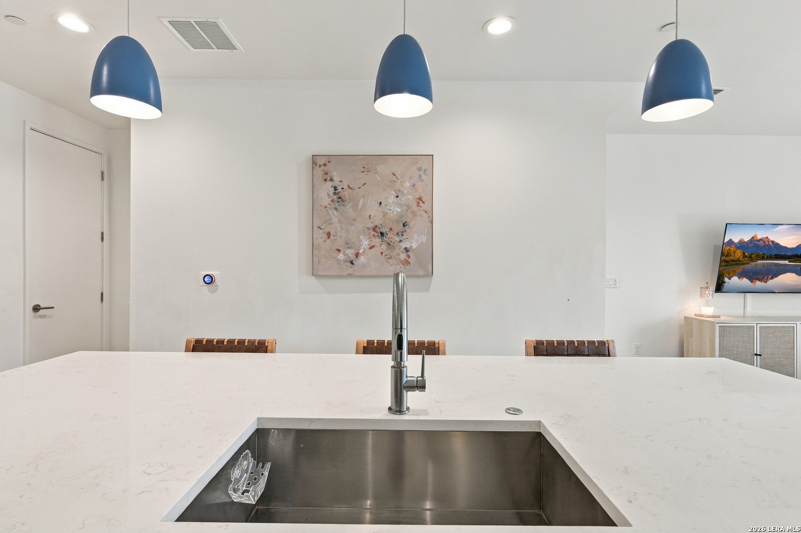 Modern kitchen with a white quartz island, large stainless-steel sink, and three blue pendant lights.