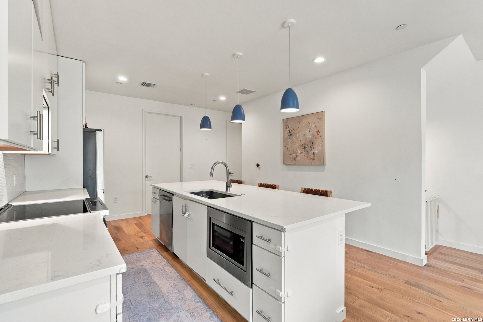 Modern kitchen with a large white island, built-in microwave, stainless steel appliances, and blue pendant lights.
