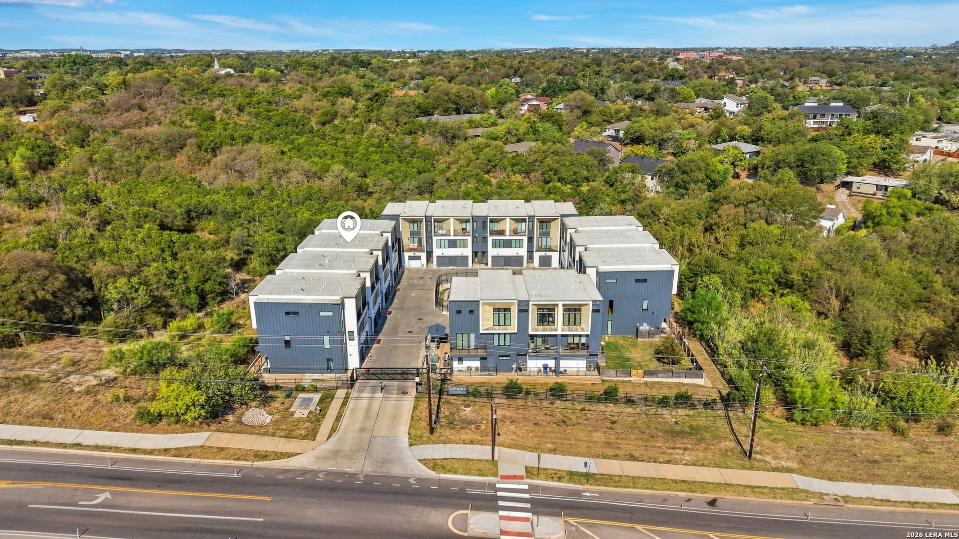 Aerial view of a modern blue-and-white residential complex with a central courtyard and tree-lined surroundings.