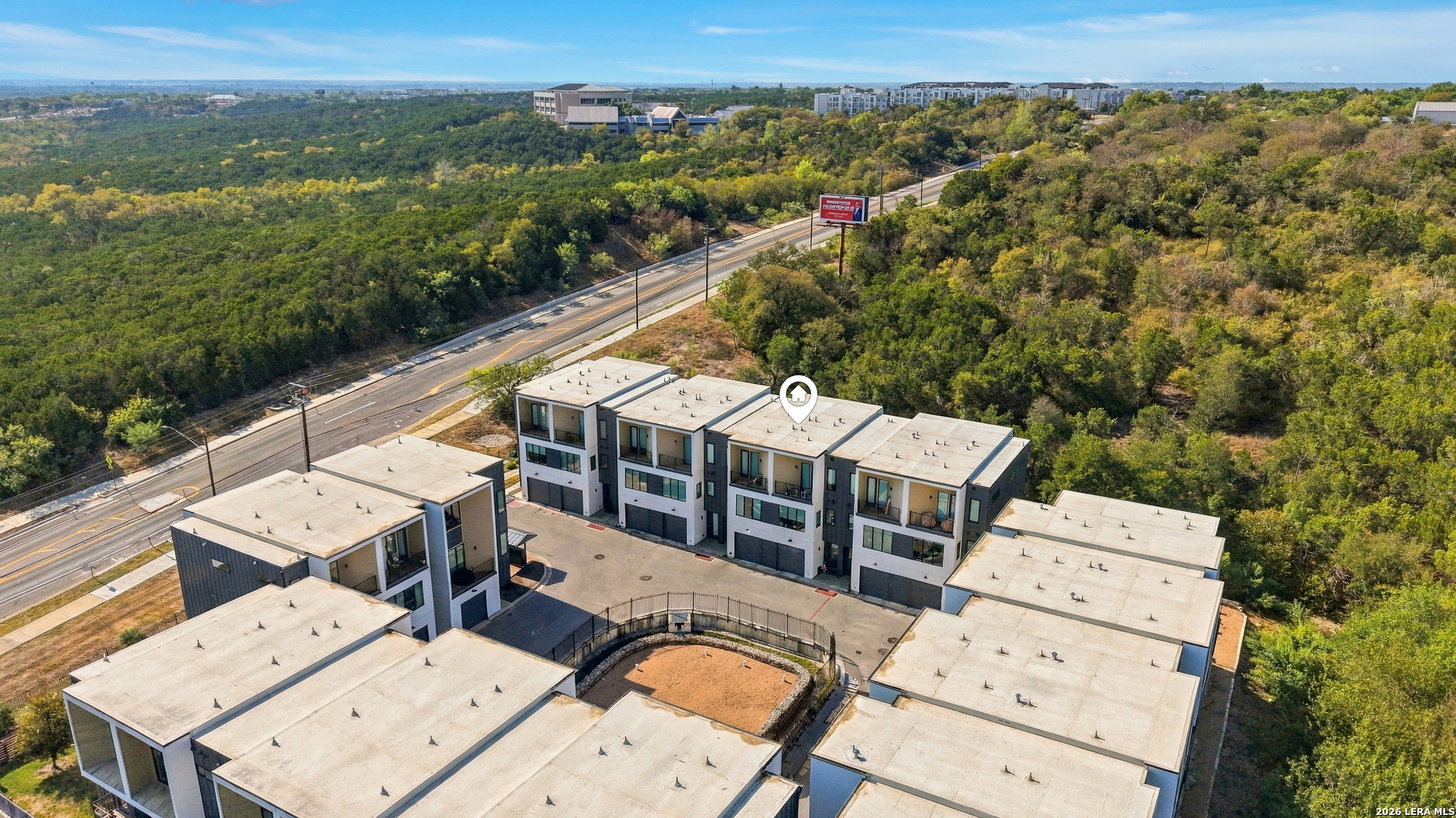 Aerial view of modern townhomes surrounding a courtyard beside a wooded landscape.