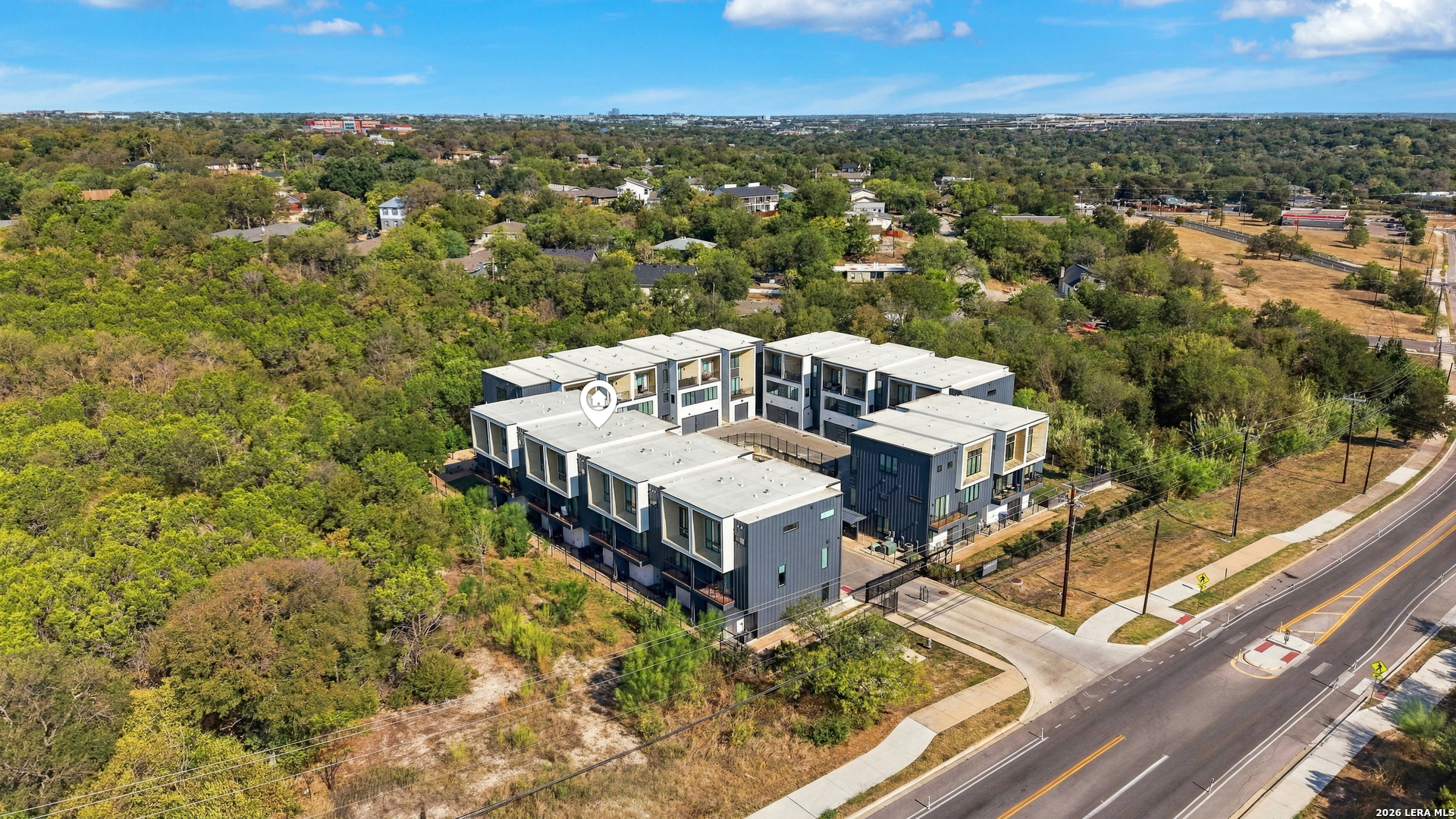 Aerial view of modern townhomes arranged around a courtyard, bordered by trees and a road.