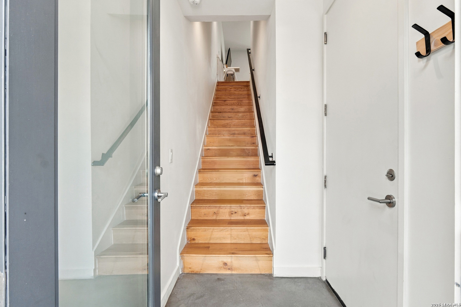 Entryway with a straight wooden staircase, glass-paneled door, and gray concrete floor.