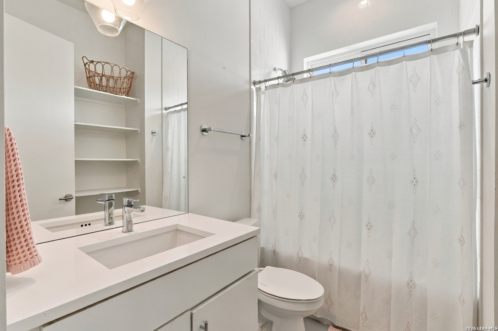 Bathroom with a white vanity, mirrored wall, open shelves, and a patterned shower curtain.