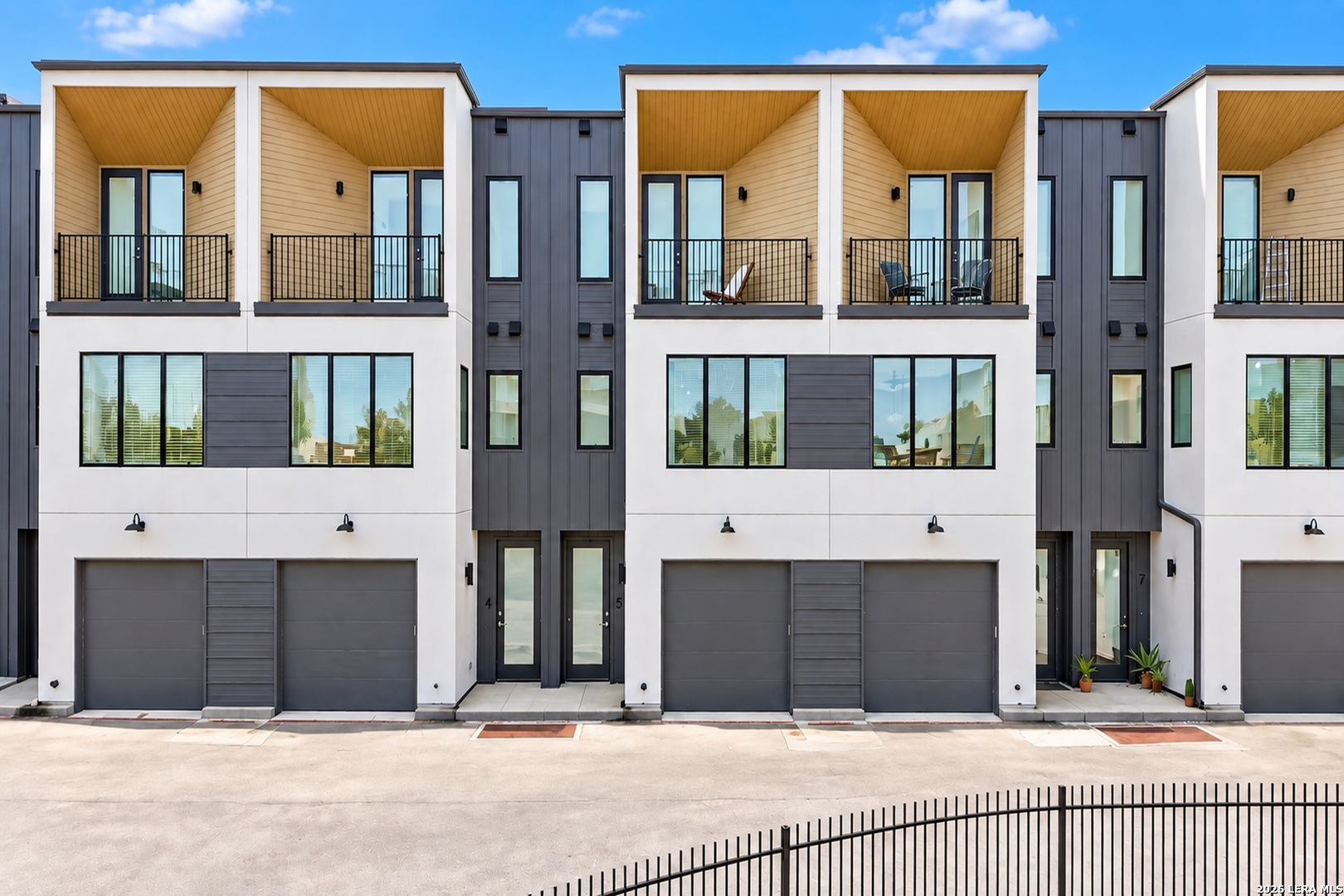 Modern townhomes with white and charcoal facades, upper balconies, and ground-level garages.