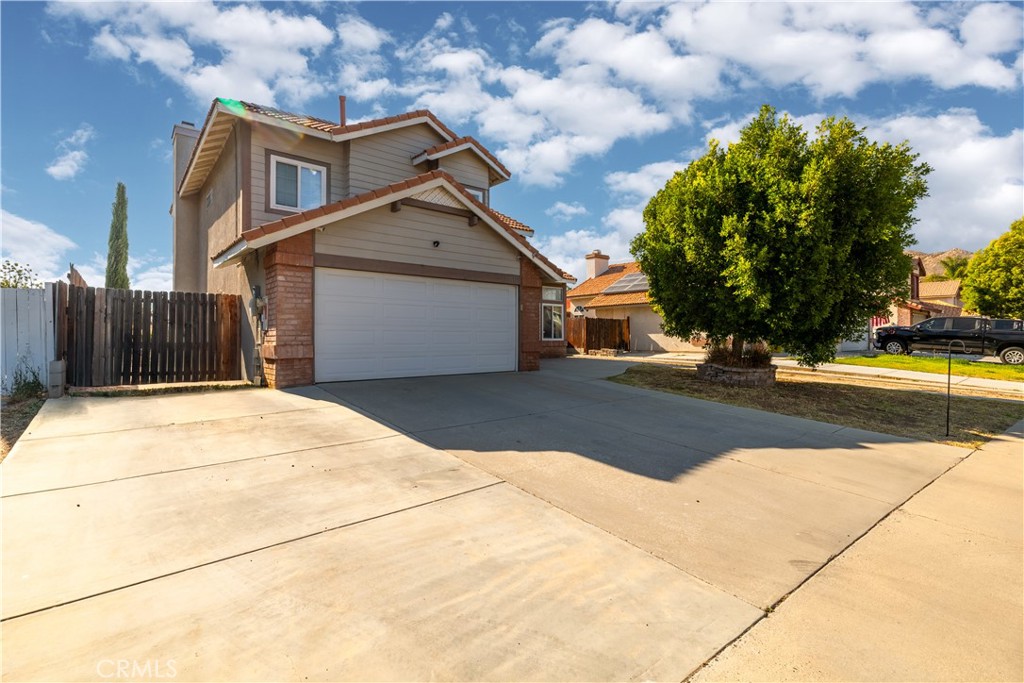 Two-story house with a double garage, wide concrete driveway, and large leafy tree in the front yard.