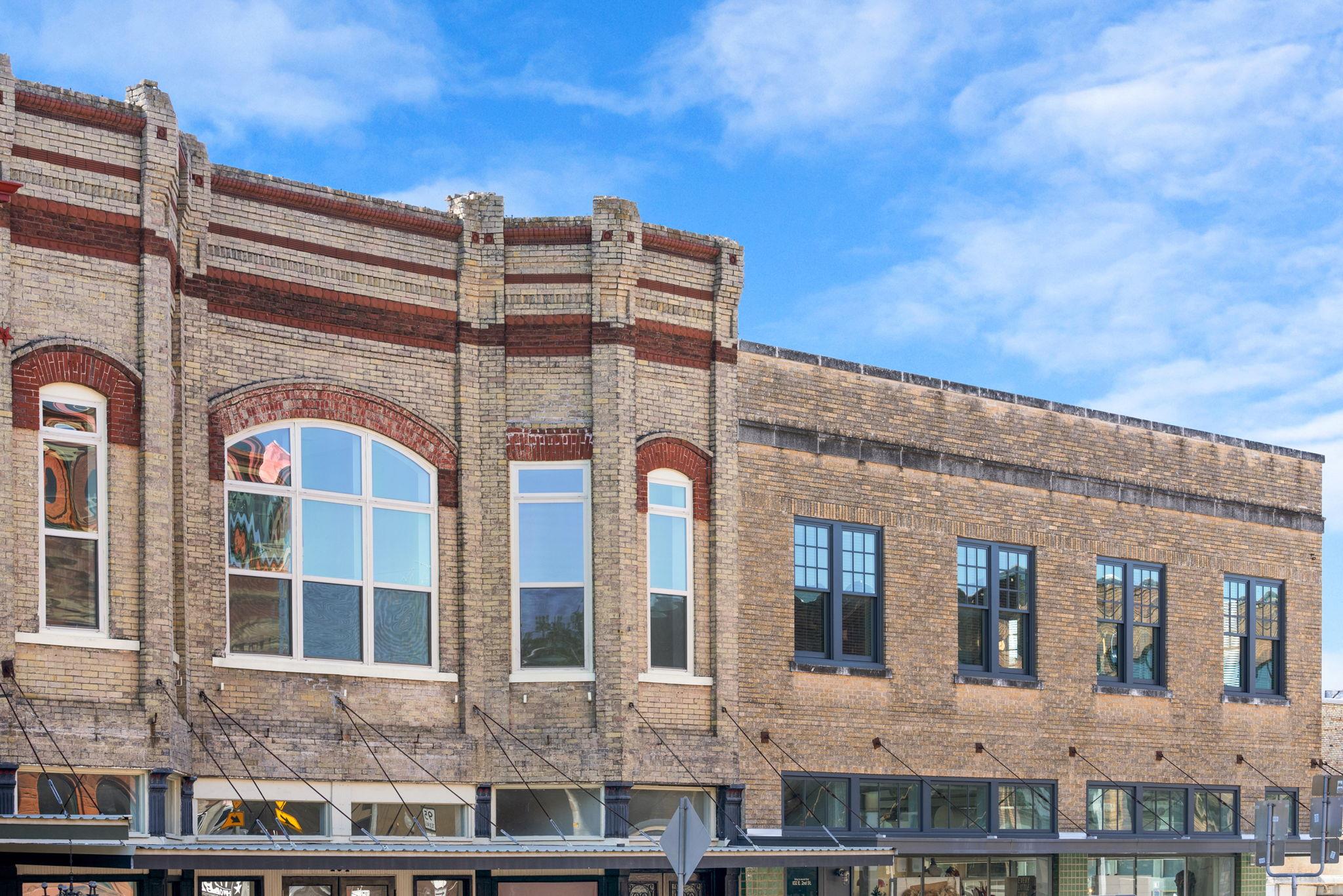Historic brick commercial building with red accents, arched windows, and rows of dark-framed windows.