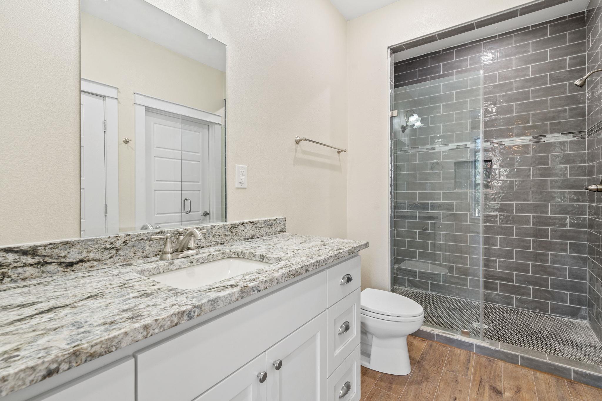 Bathroom with a stone-counter vanity and glass-enclosed dark gray tiled shower.