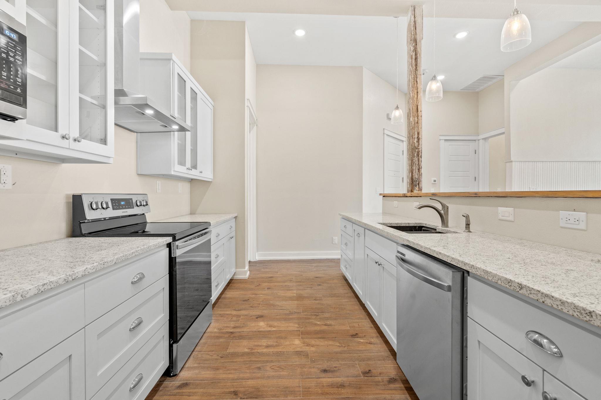 Modern kitchen with white cabinets, stainless steel appliances, speckled countertops, and warm wood-look floors.