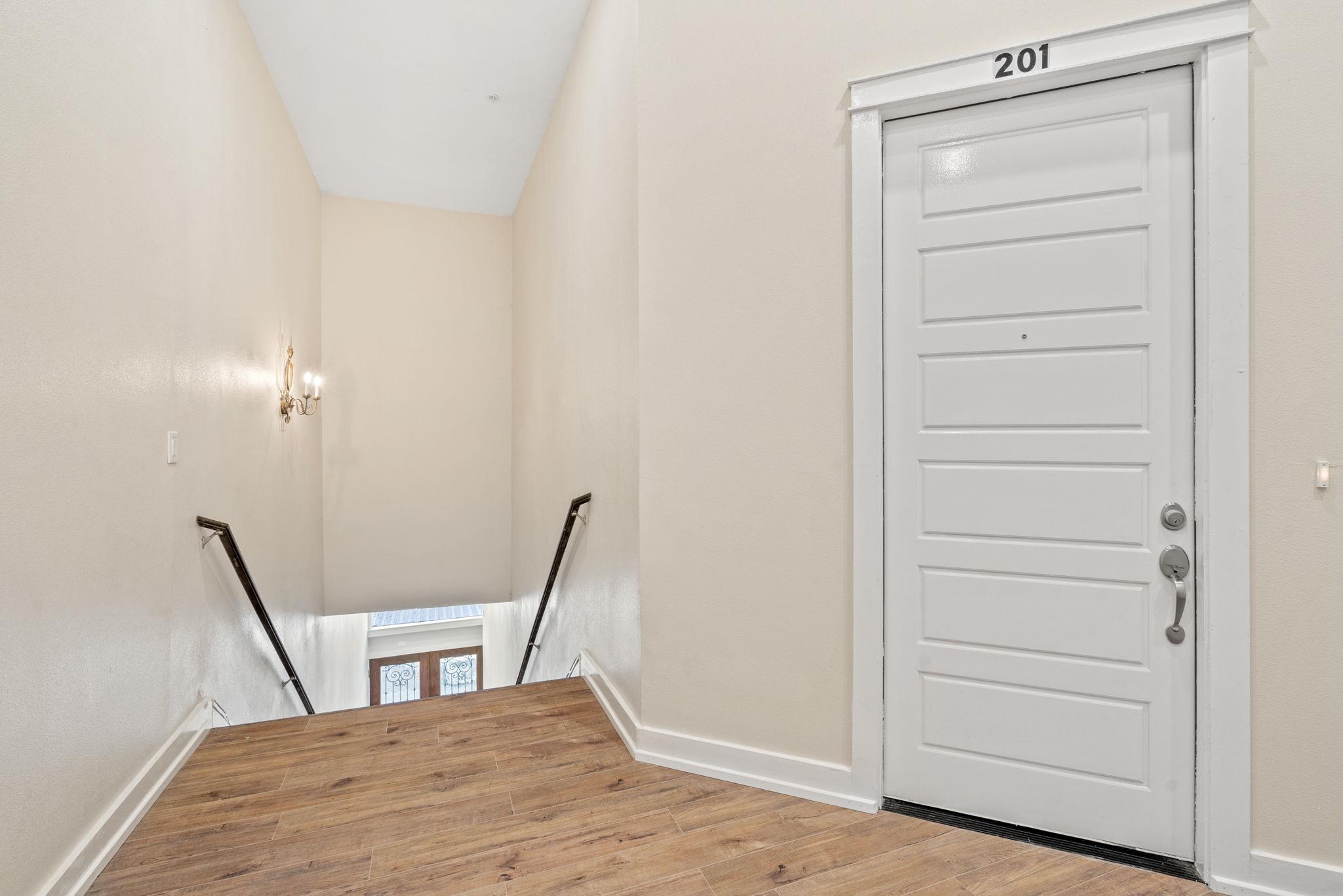 Entry landing with a white door marked 201 beside a stairwell and wood-look flooring.