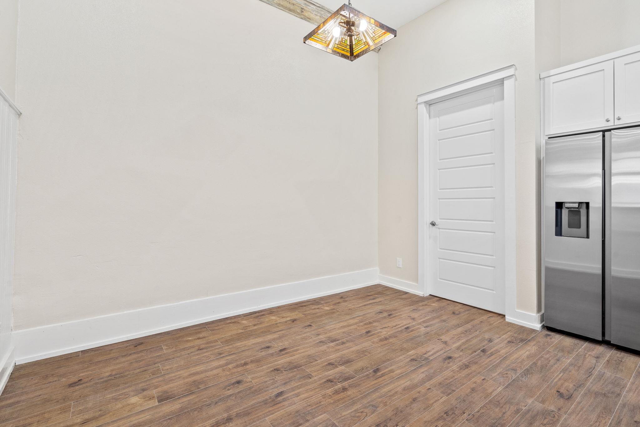 Unfurnished room with wood-look flooring, a paneled door, stainless steel refrigerator, and stained-glass pendant light.