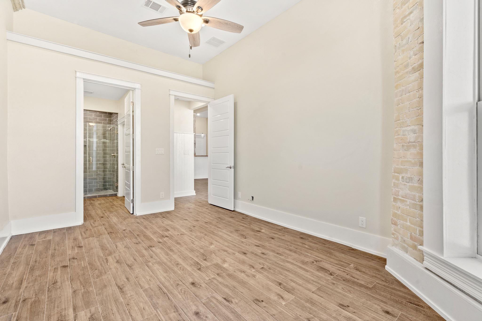 Empty room with wood-look tile floors, a ceiling fan, and an exposed brick wall.