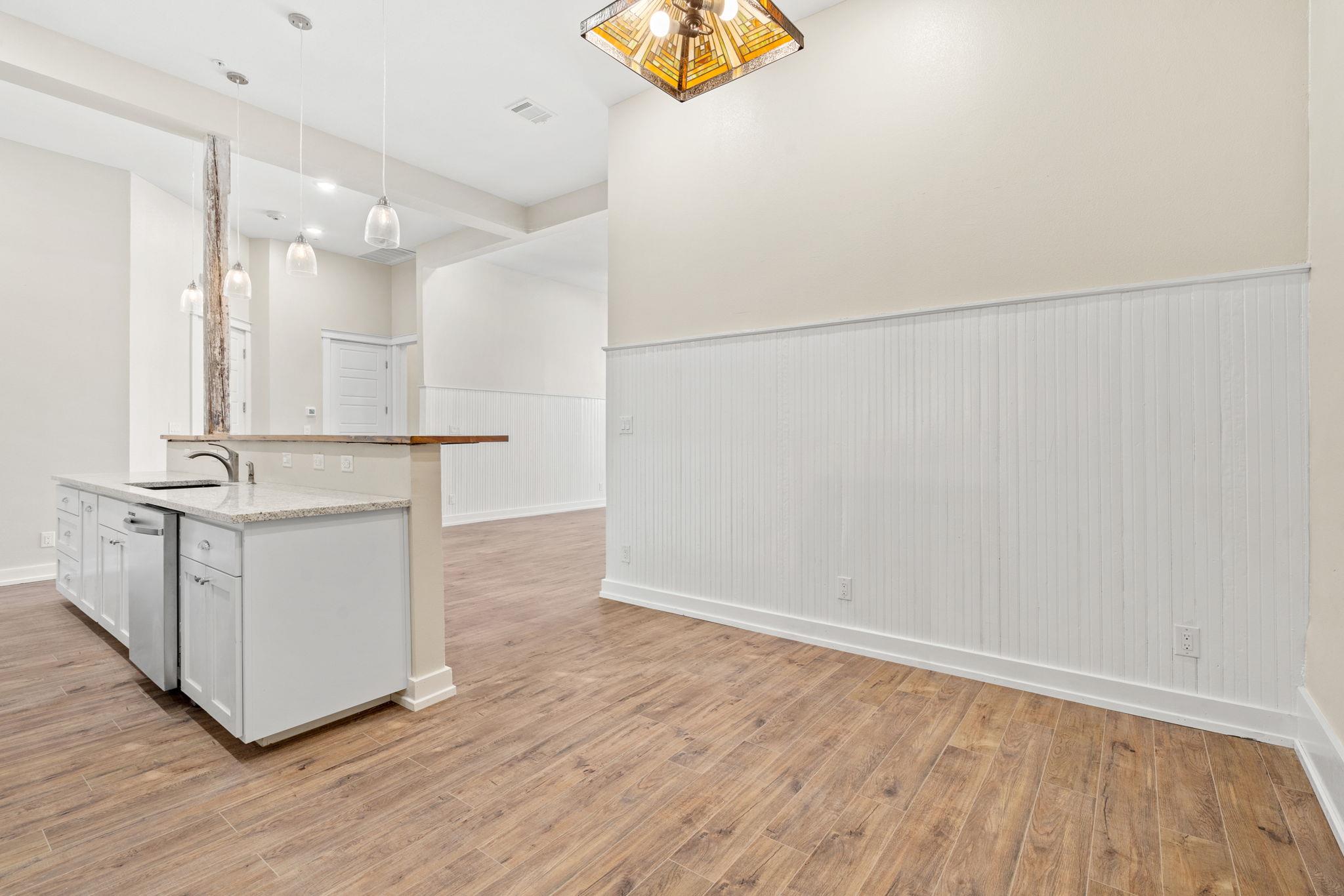 Open kitchen with white cabinets, granite counters, wood-look flooring, and pendant lights.