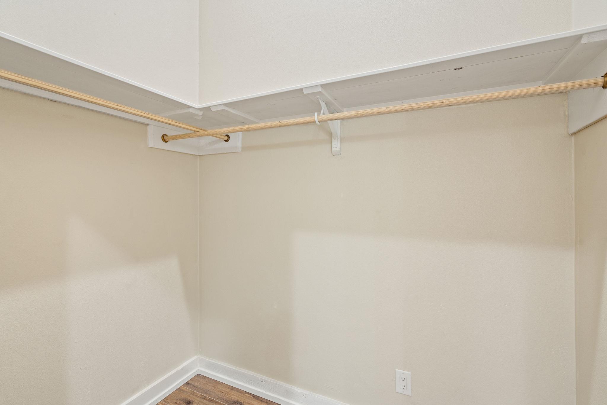 Empty closet with a wooden clothes rod and brown wood flooring.