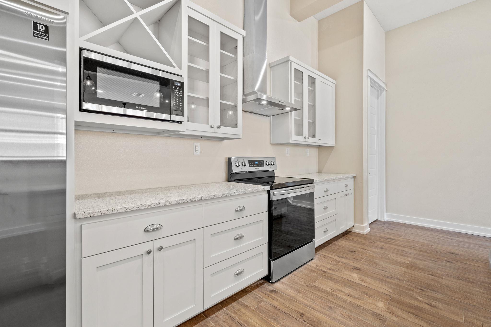 Kitchen with white cabinets, stainless steel appliances, speckled countertops, and wood-look flooring.