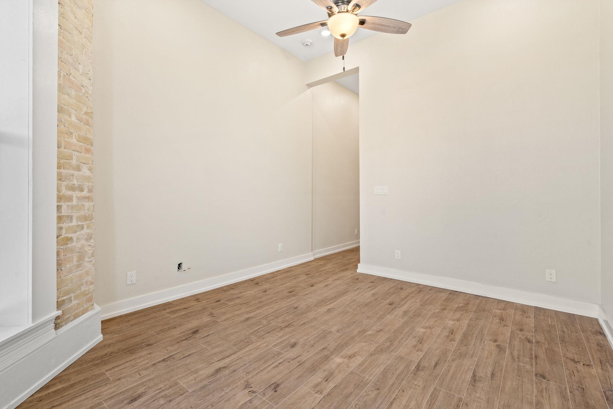 Vacant room with wood-look flooring, a brick accent wall, and a ceiling fan with light.
