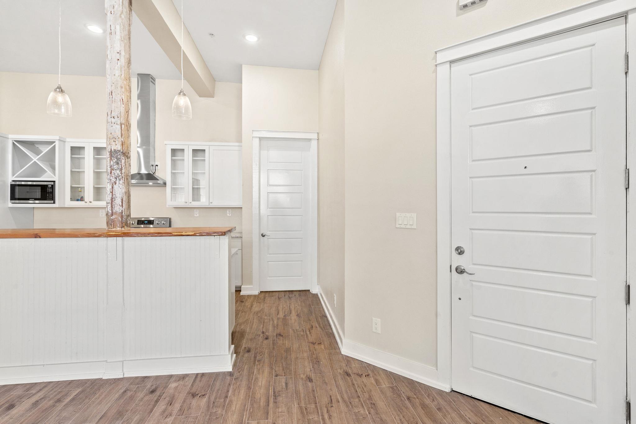 Kitchen and entry with white cabinetry, wood-topped peninsula, and exposed weathered support post.