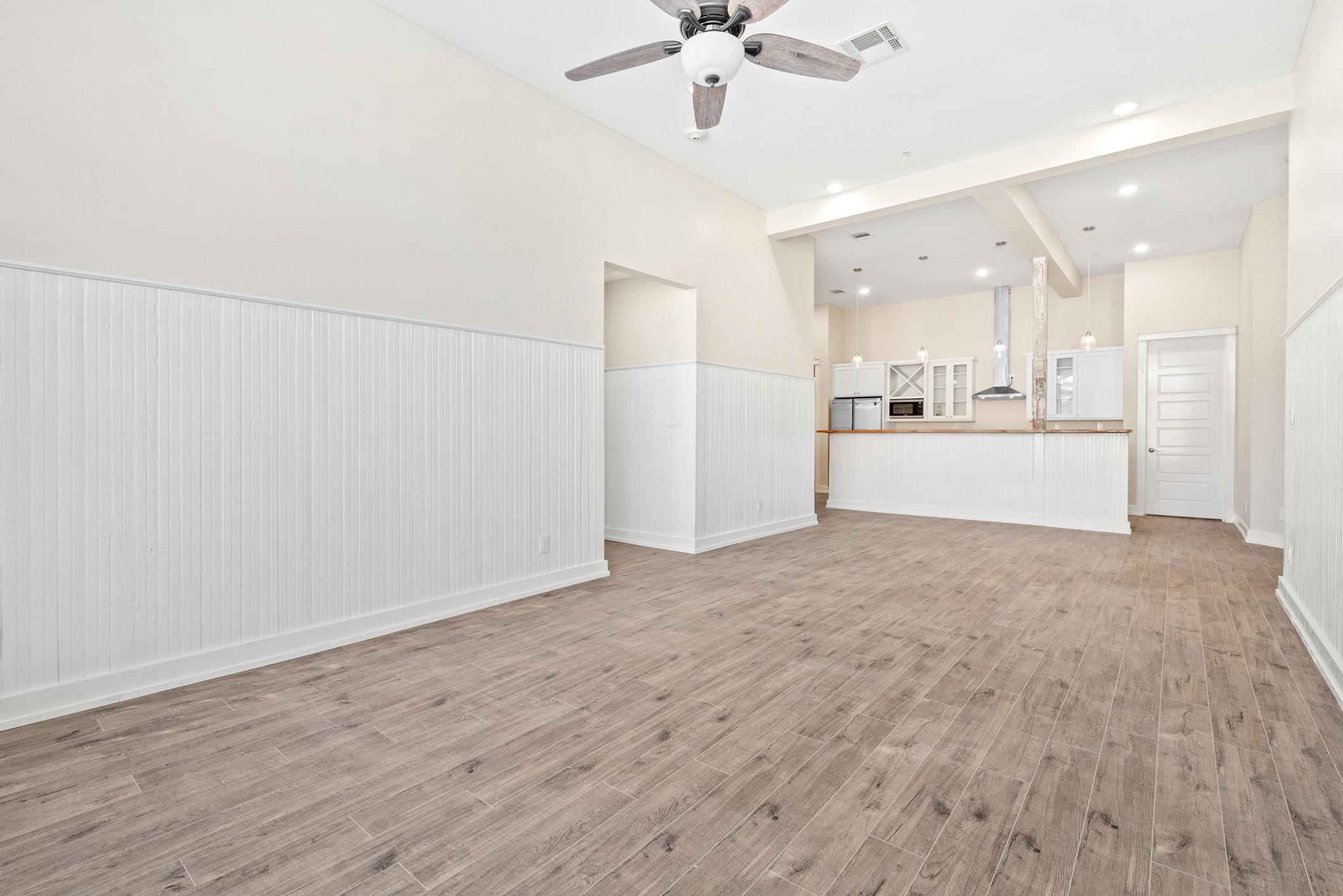 Open living area with wood-look floors, white beadboard walls, and a kitchen breakfast bar.