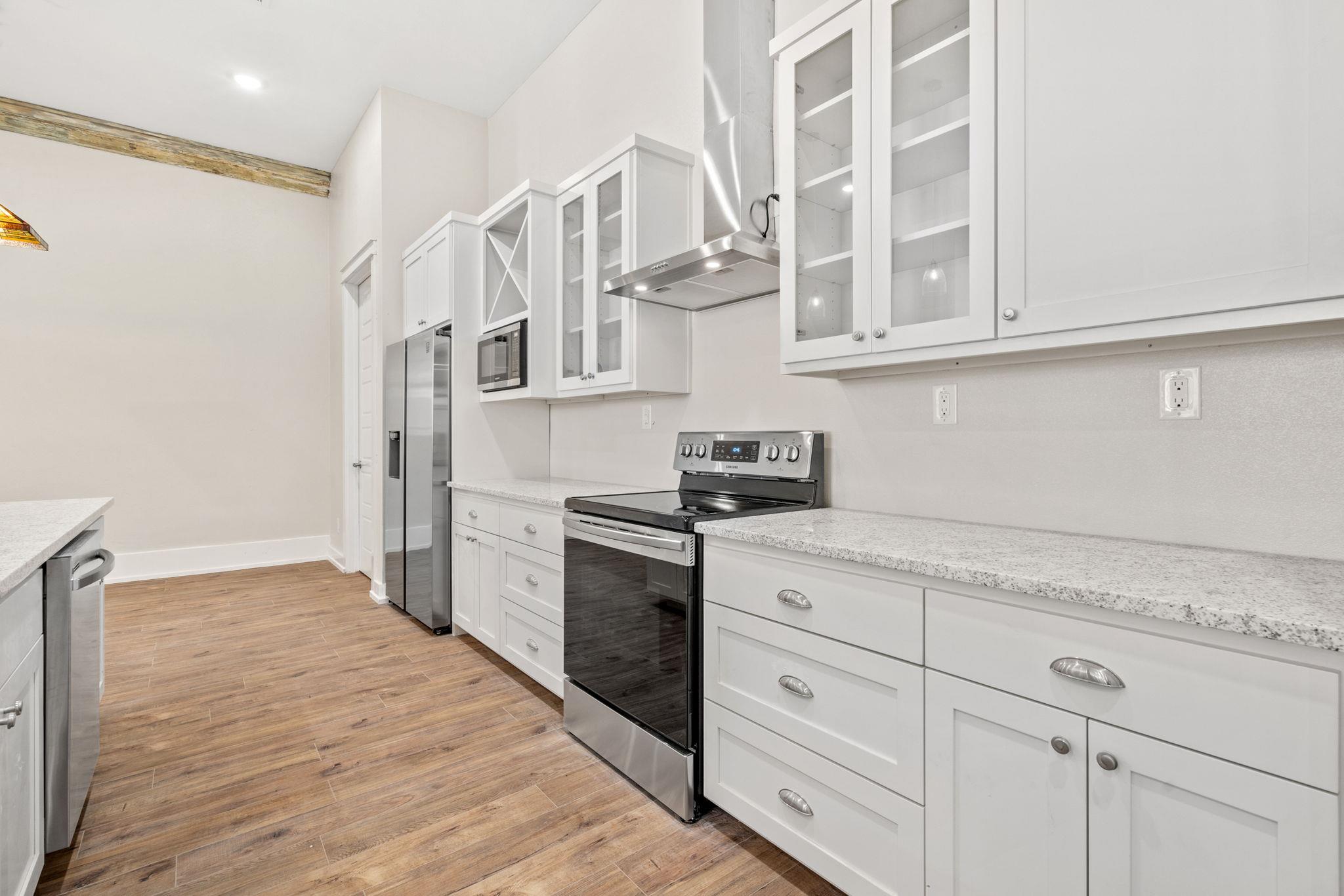 Kitchen with white cabinets, stainless steel appliances, stone countertops, and warm wood-look flooring.